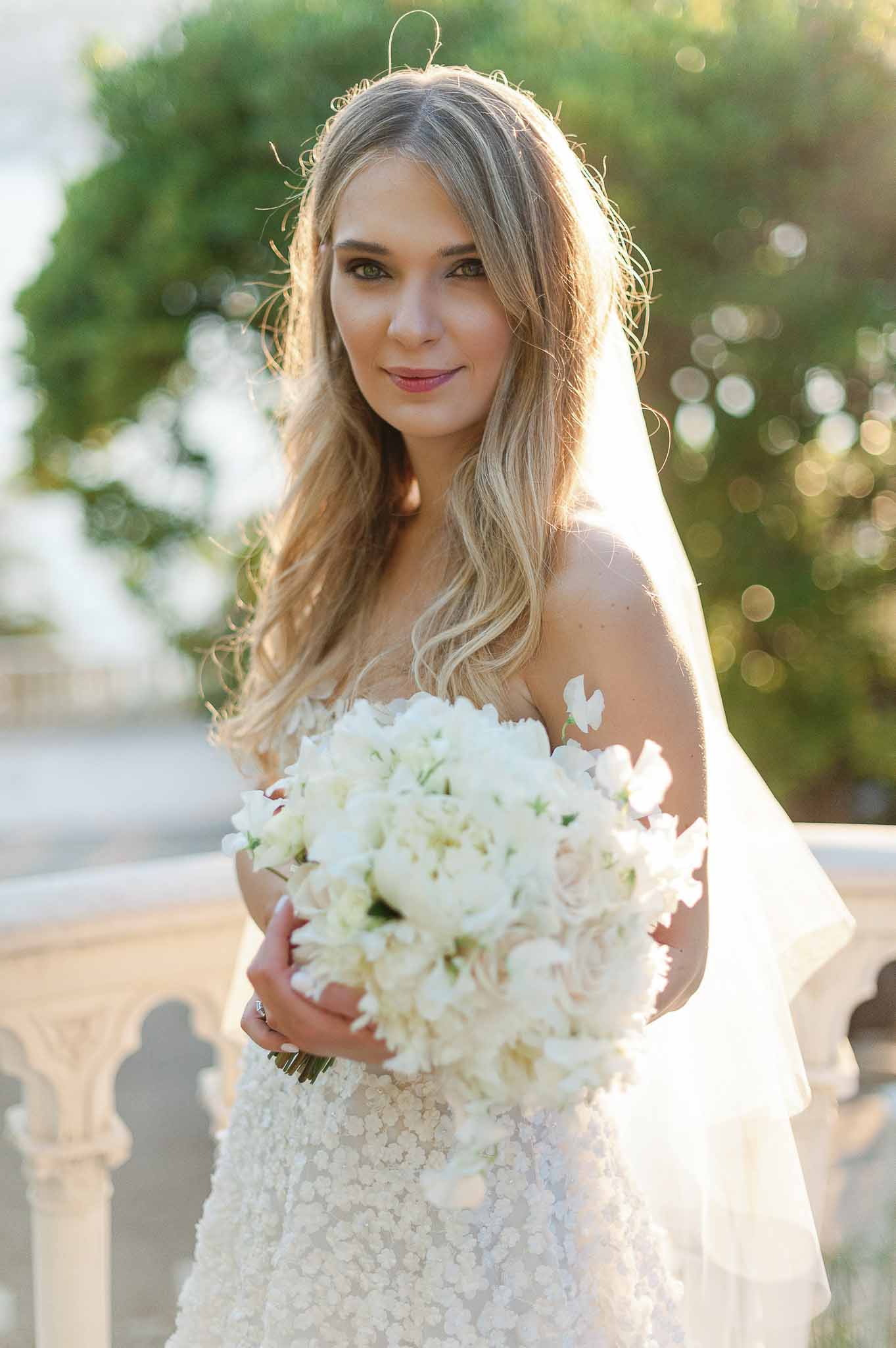 Bride in ivory beaded gown holding white hydrangea bouquet outdoors in golden hour light