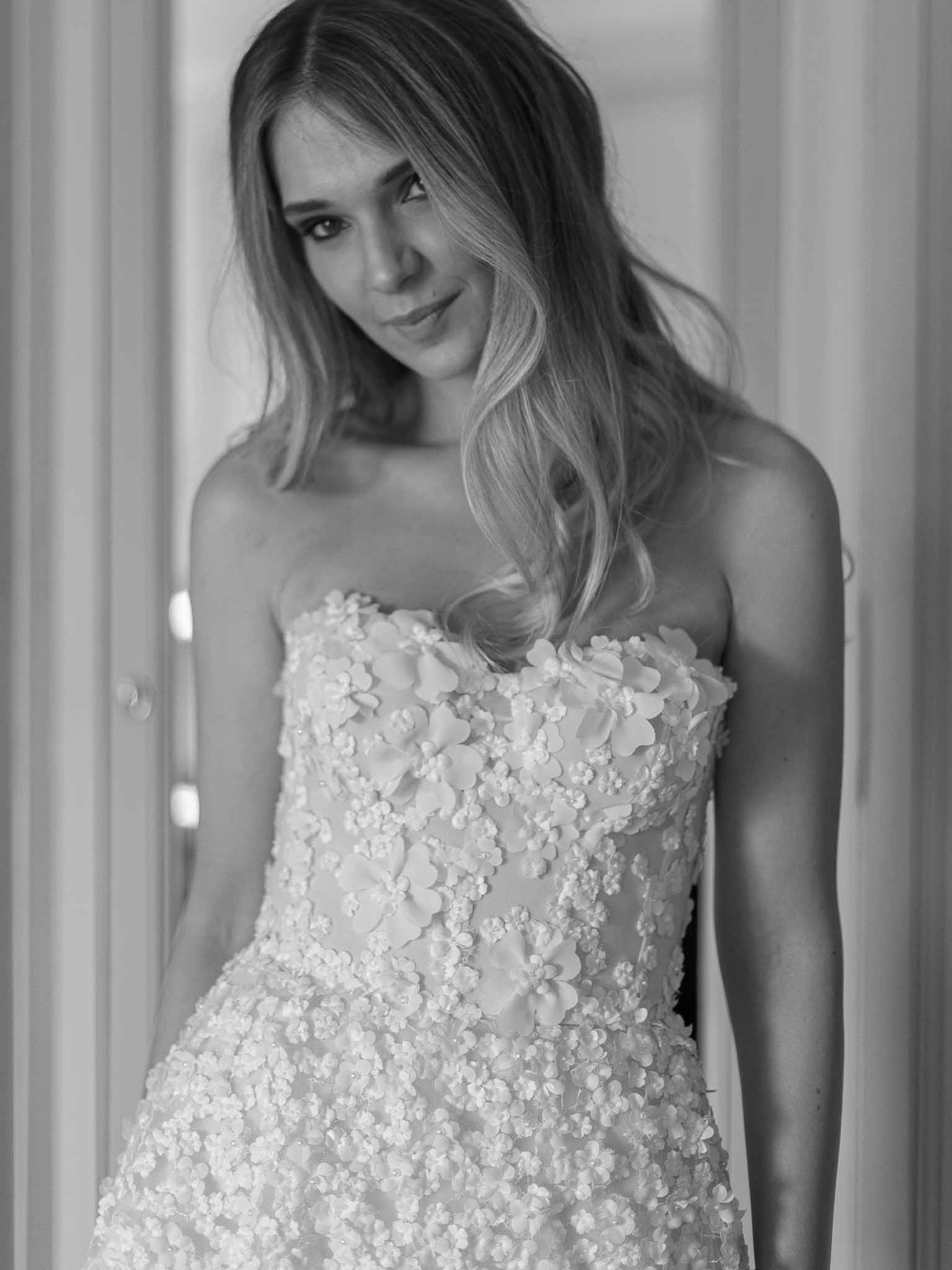 Black and white bridal portrait showcasing textured wedding dress with floral appliqués indoors