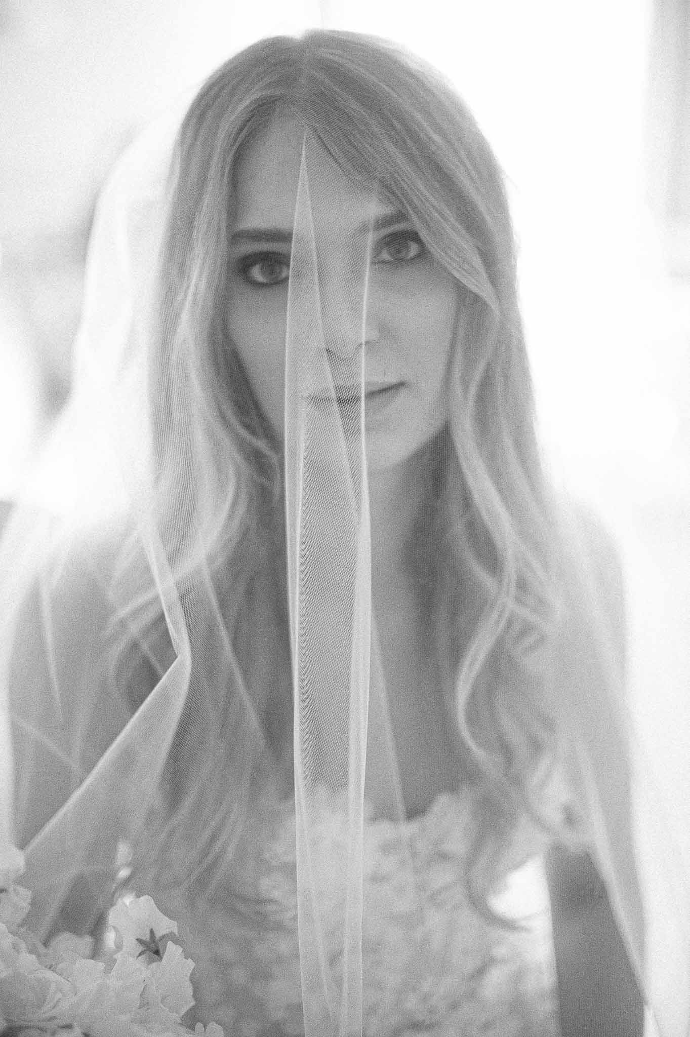 Black and white bridal portrait with bride behind sheer veil holding bouquet