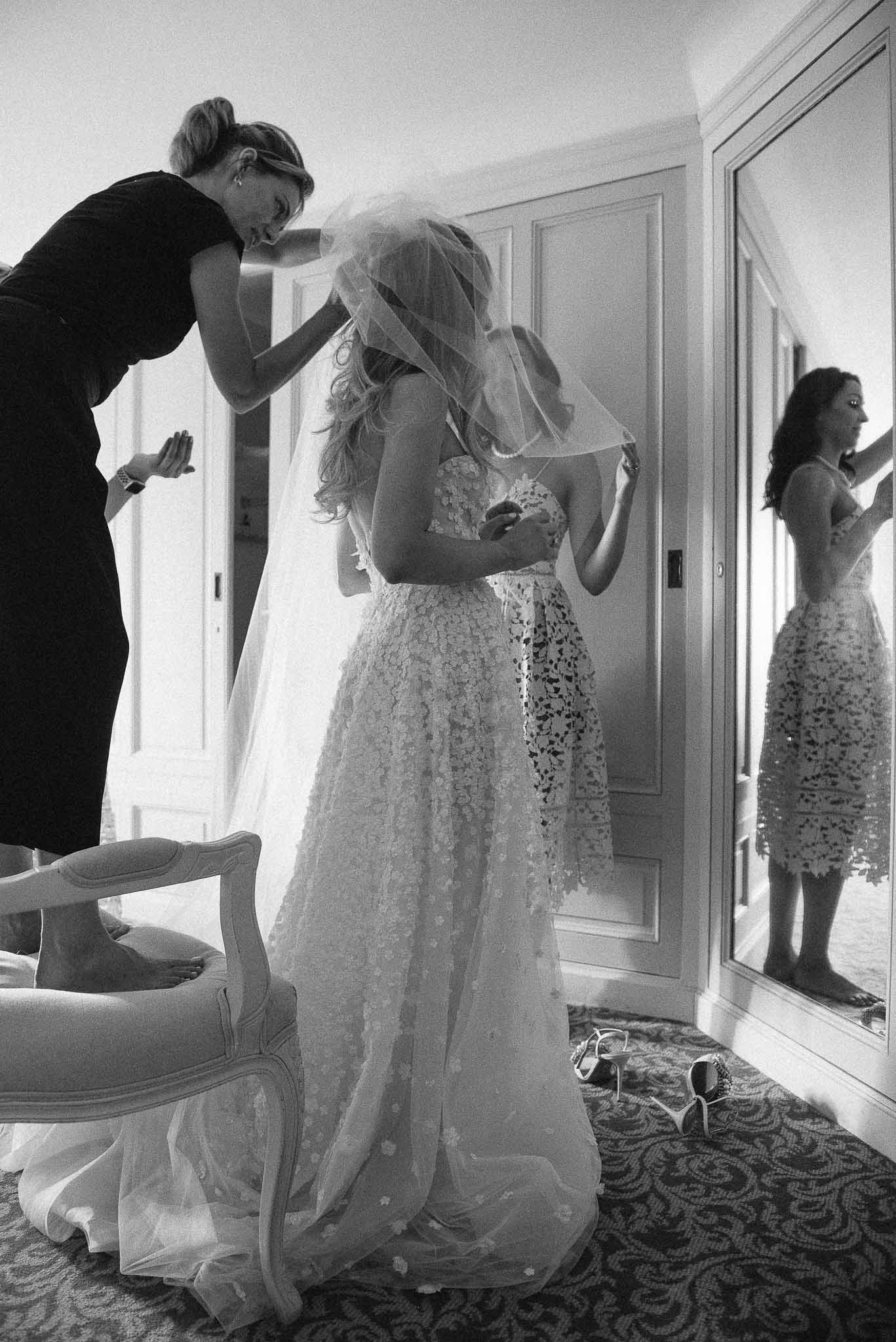 Bride getting veil adjusted by attendants in bright bridal suite during wedding preparation