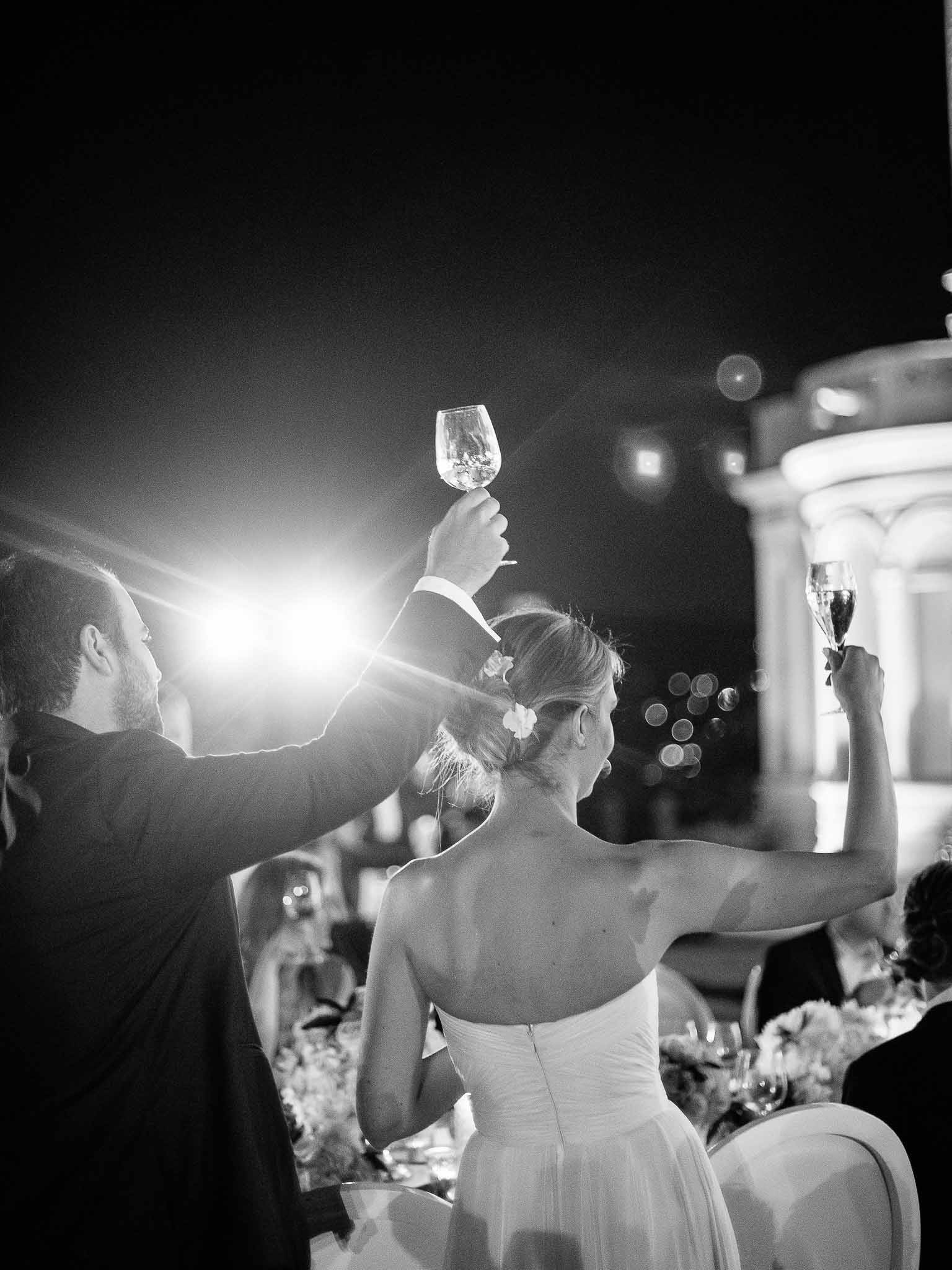 Bride and groom raising glasses during nighttime reception toasts at outdoor wedding venue