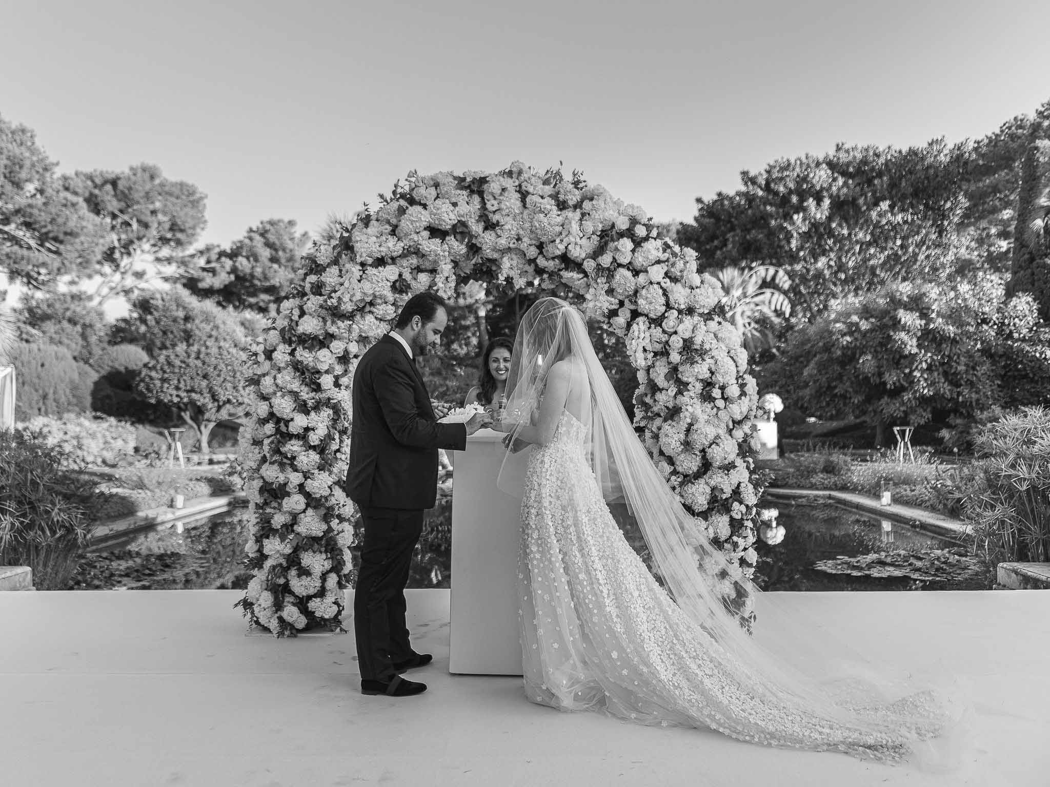 Wedding ceremony with couple and officiant under floral arch in garden setting