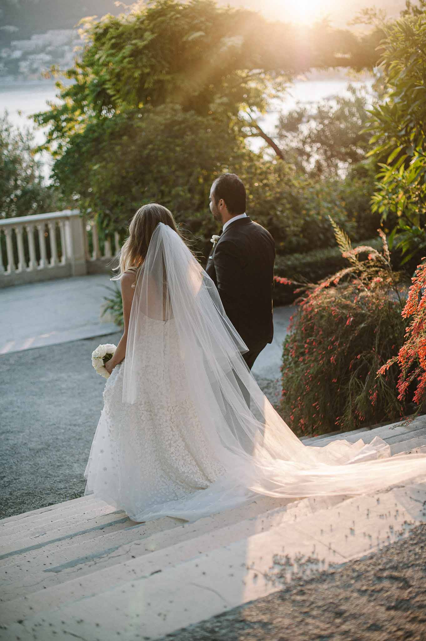 Bride and groom walking together on stone terrace at garden estate during golden hour