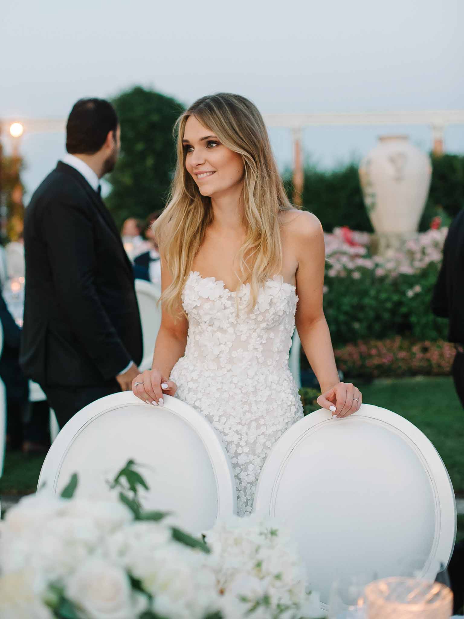 Bride in ivory gown with floral appliqués posing at outdoor garden reception venue