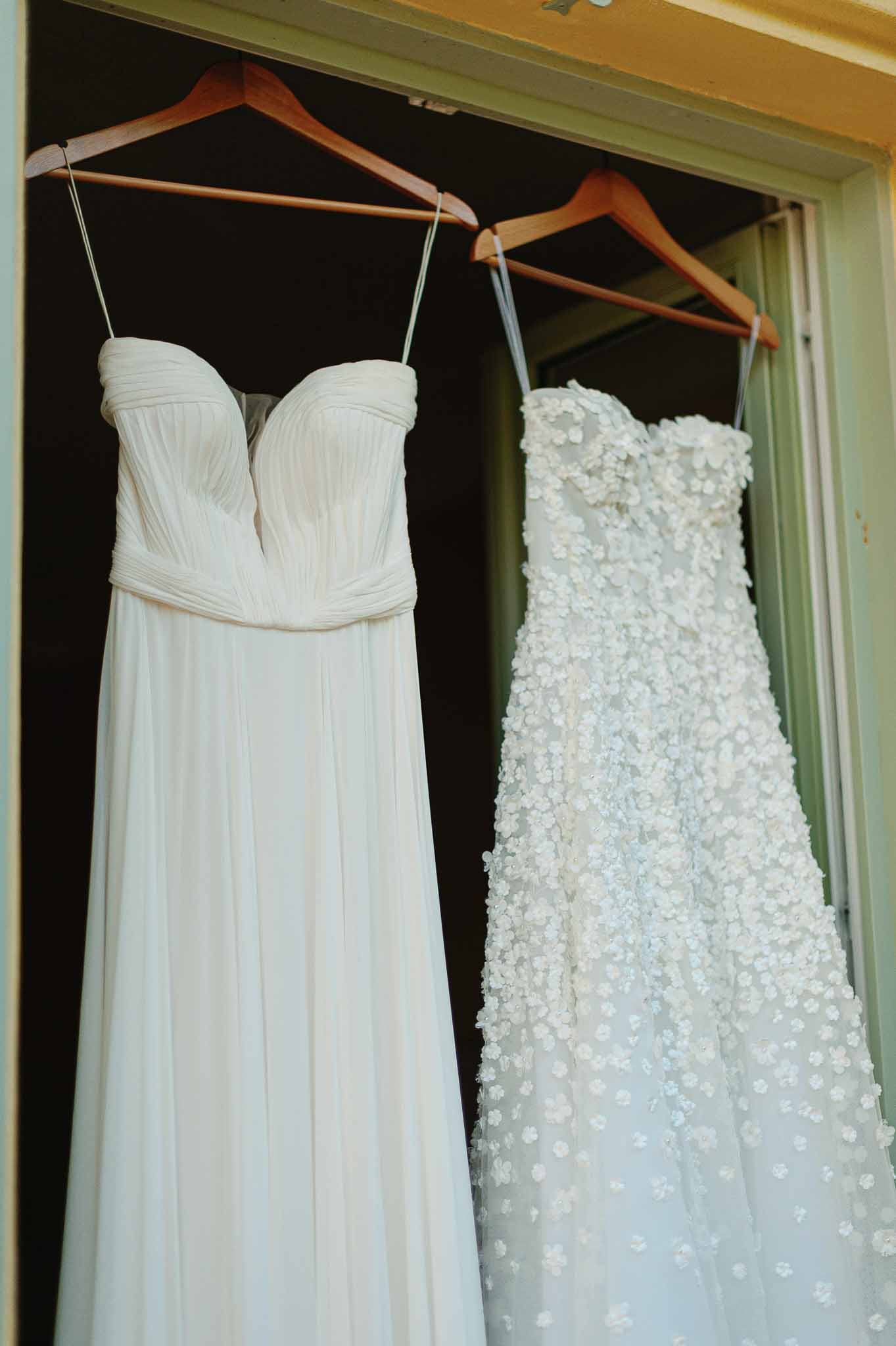Two ivory wedding dresses hanging on wooden hangers during bridal preparation