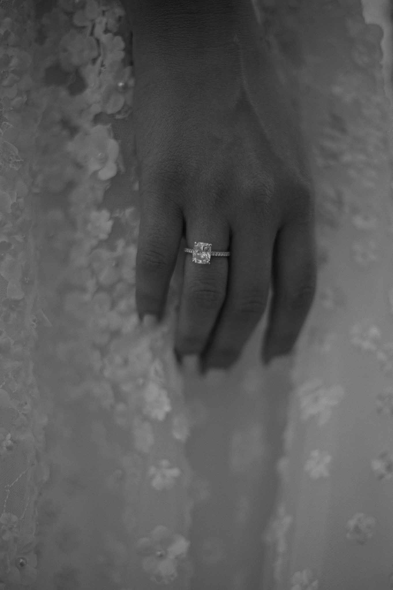Bride's engagement and wedding rings on hand against lace wedding dress fabric in black and white