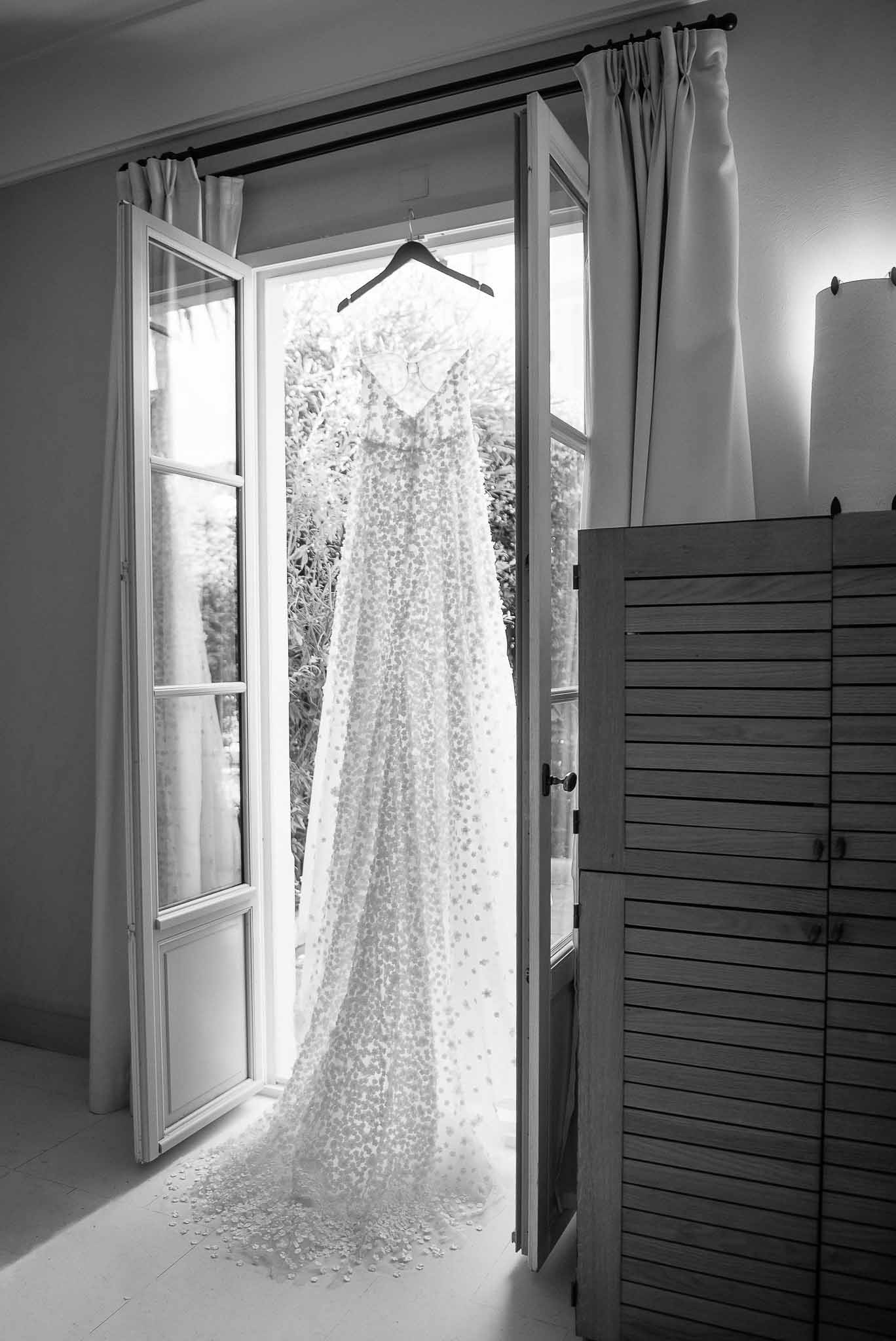 Wedding dress hanging in bridal suite with natural light from French doors