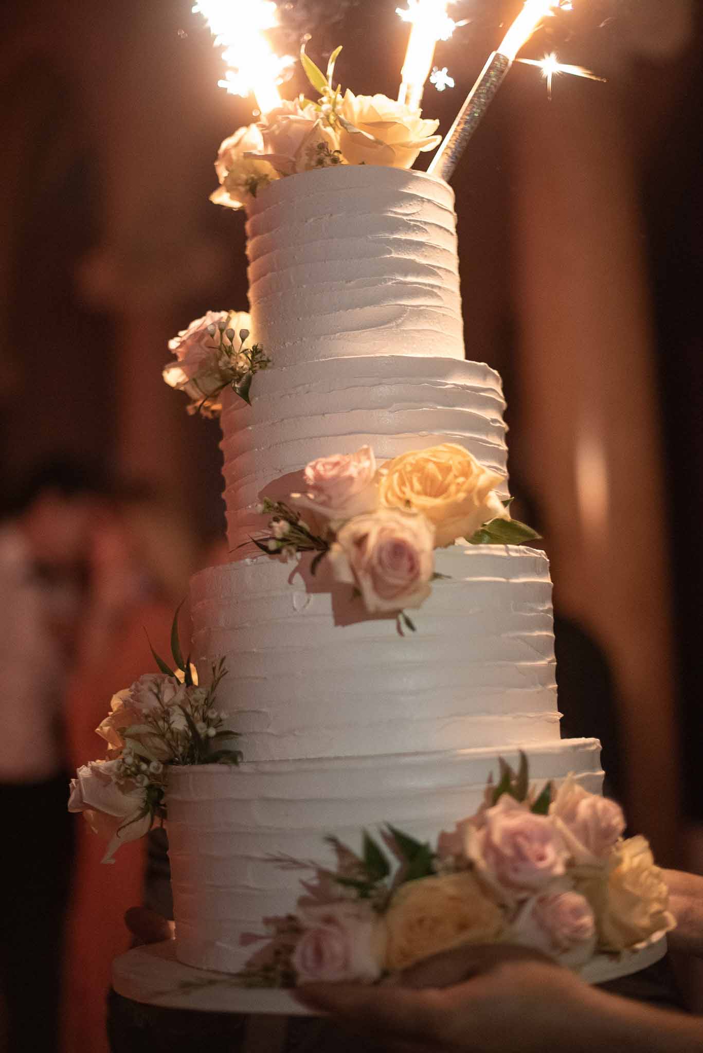 Four-tier wedding cake with sparklers and fresh flowers at evening reception