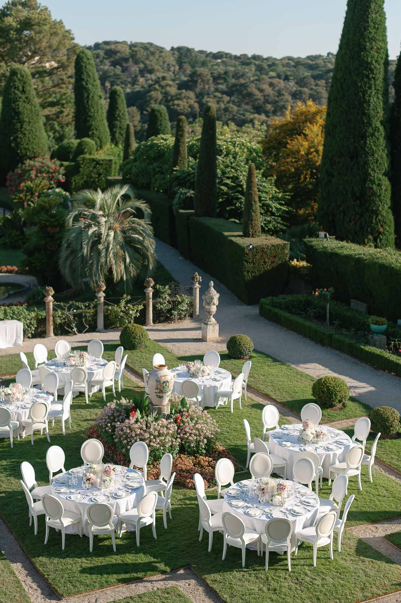 Outdoor wedding reception setup in Mediterranean garden with formal landscaping and cypress trees