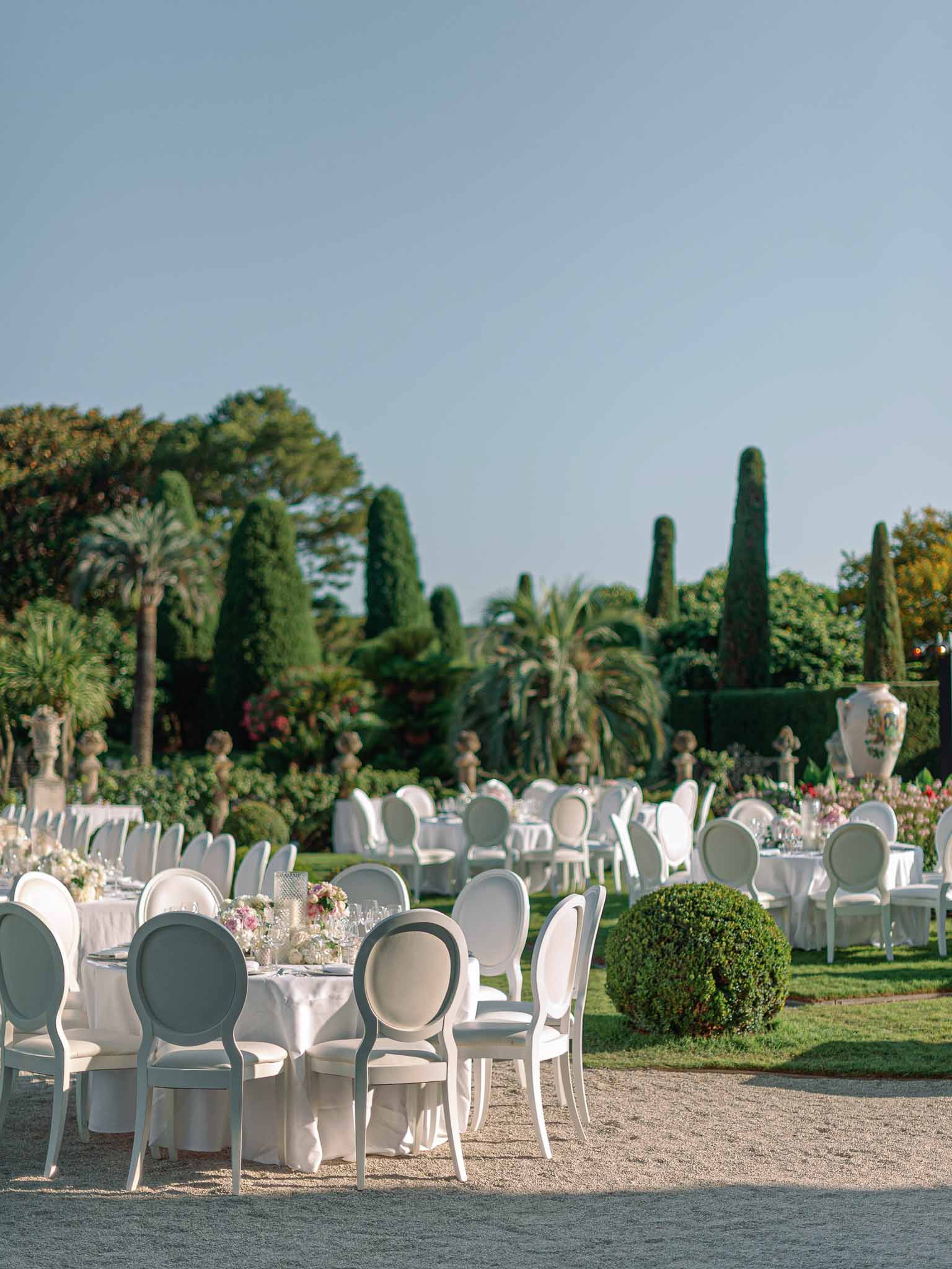 Outdoor reception table setup with white linens and floral centerpieces in formal French garden