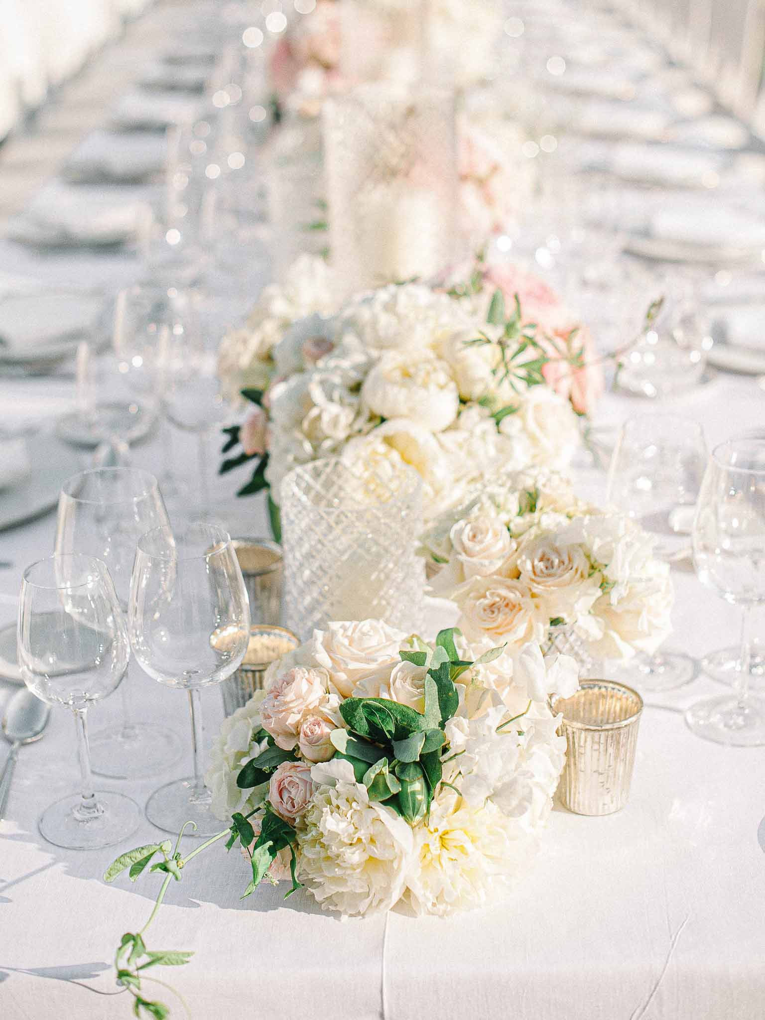 Reception table centerpiece with ivory peonies, blush roses, and gold accents at indoor wedding venue
