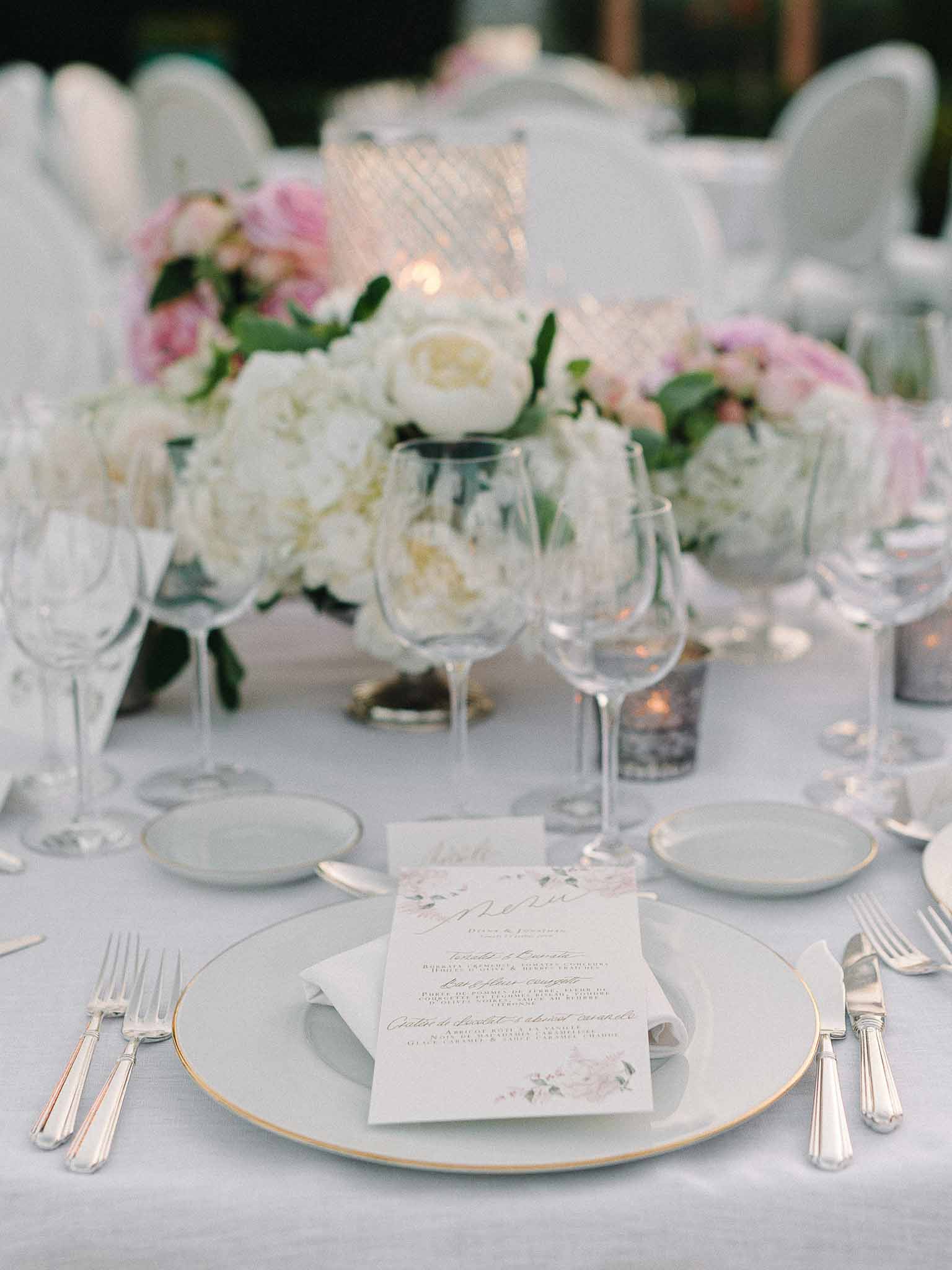 Reception table setting with place cards, floral centerpieces and gold accents at wedding venue