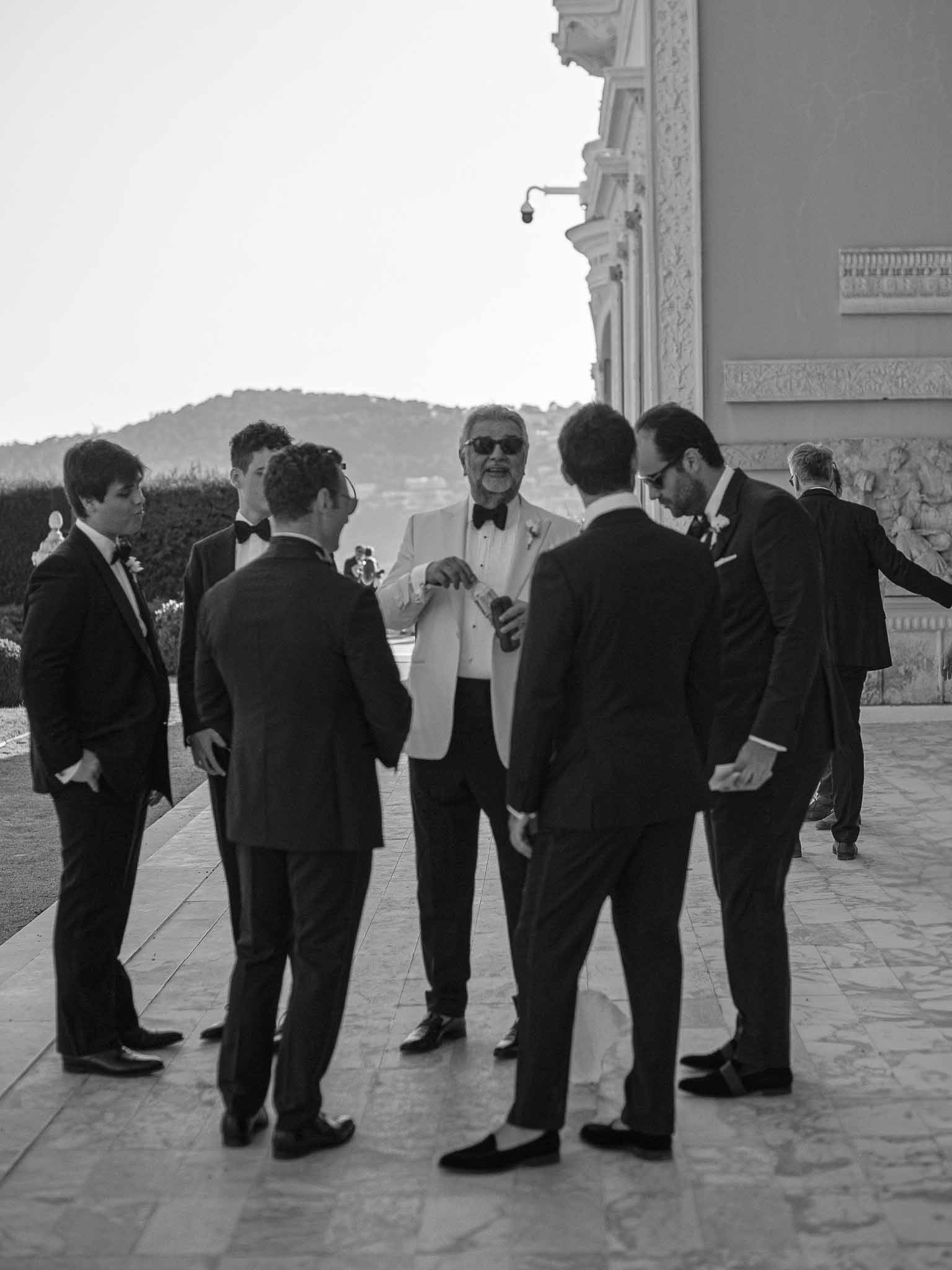 Men in formal attire gathered on stone terrace at classical venue during cocktail hour