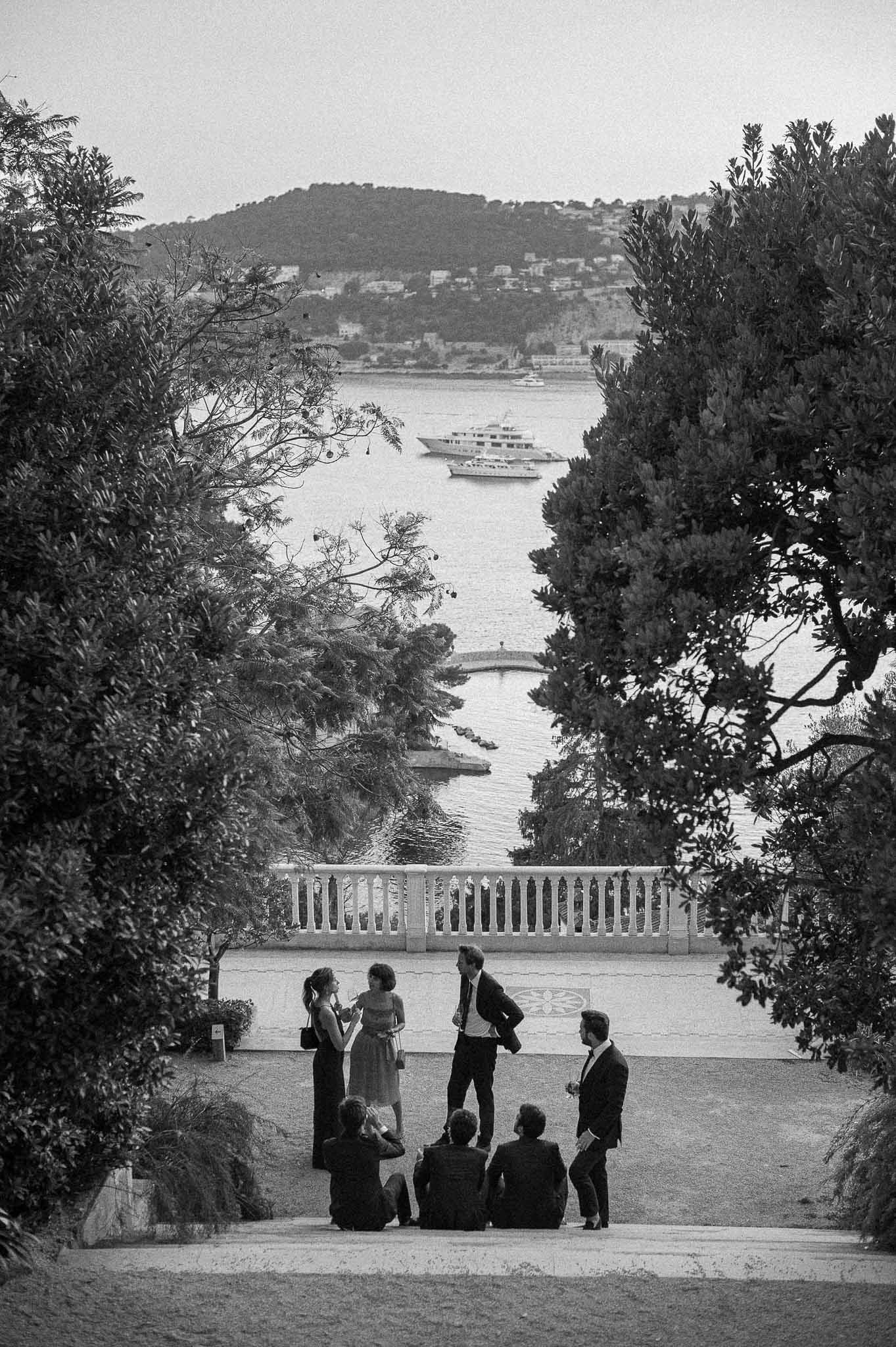 Wedding guests gathered on Mediterranean terrace overlooking harbor during cocktail hour