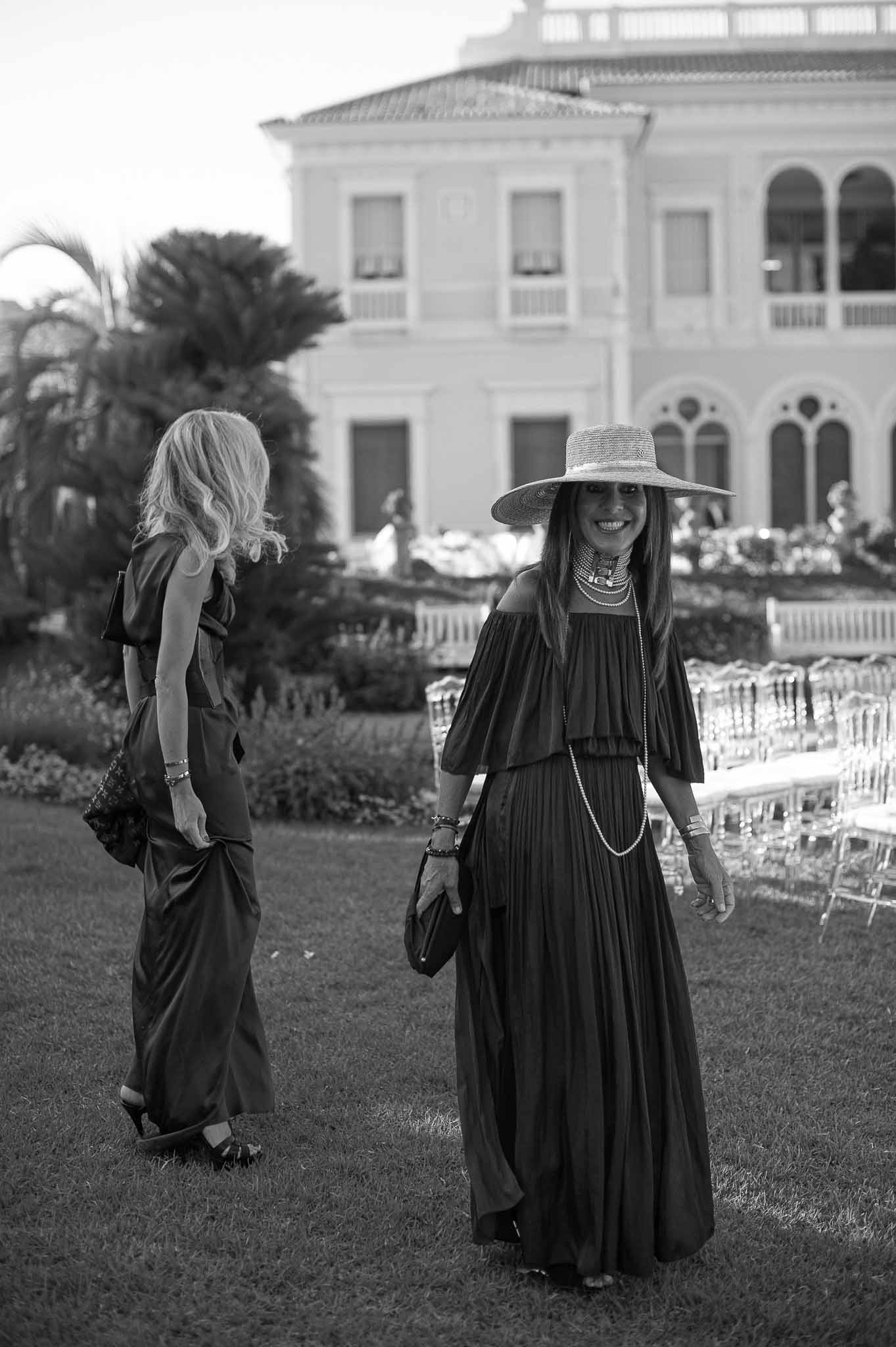 Wedding guests arriving at outdoor reception in formal garden setting with classical white building backdrop