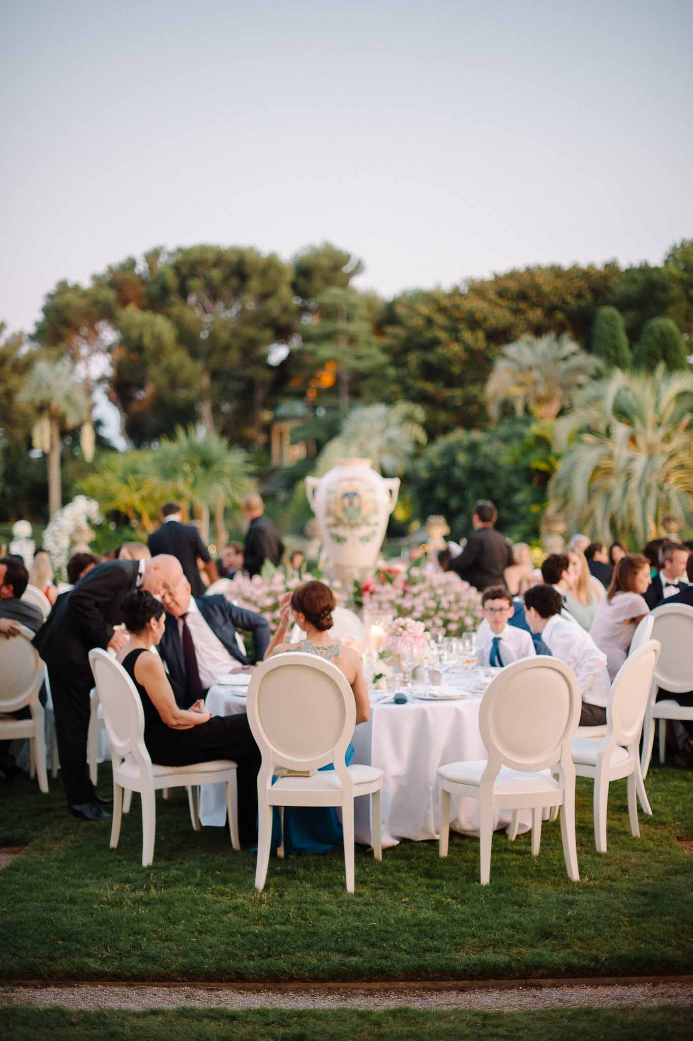 Outdoor wedding reception with guests dining at round tables in Mediterranean garden setting