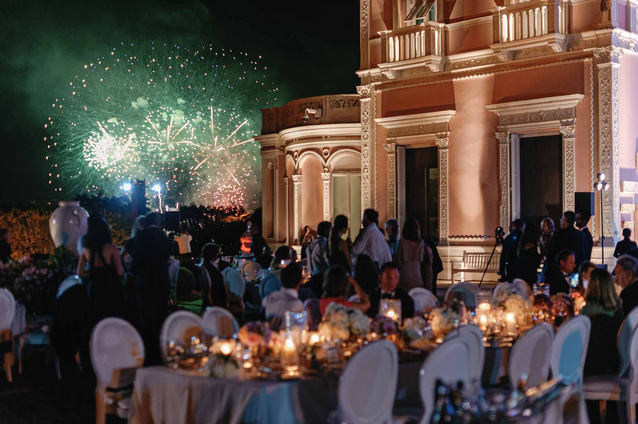 Nighttime wedding reception with fireworks display at classical venue with illuminated columns