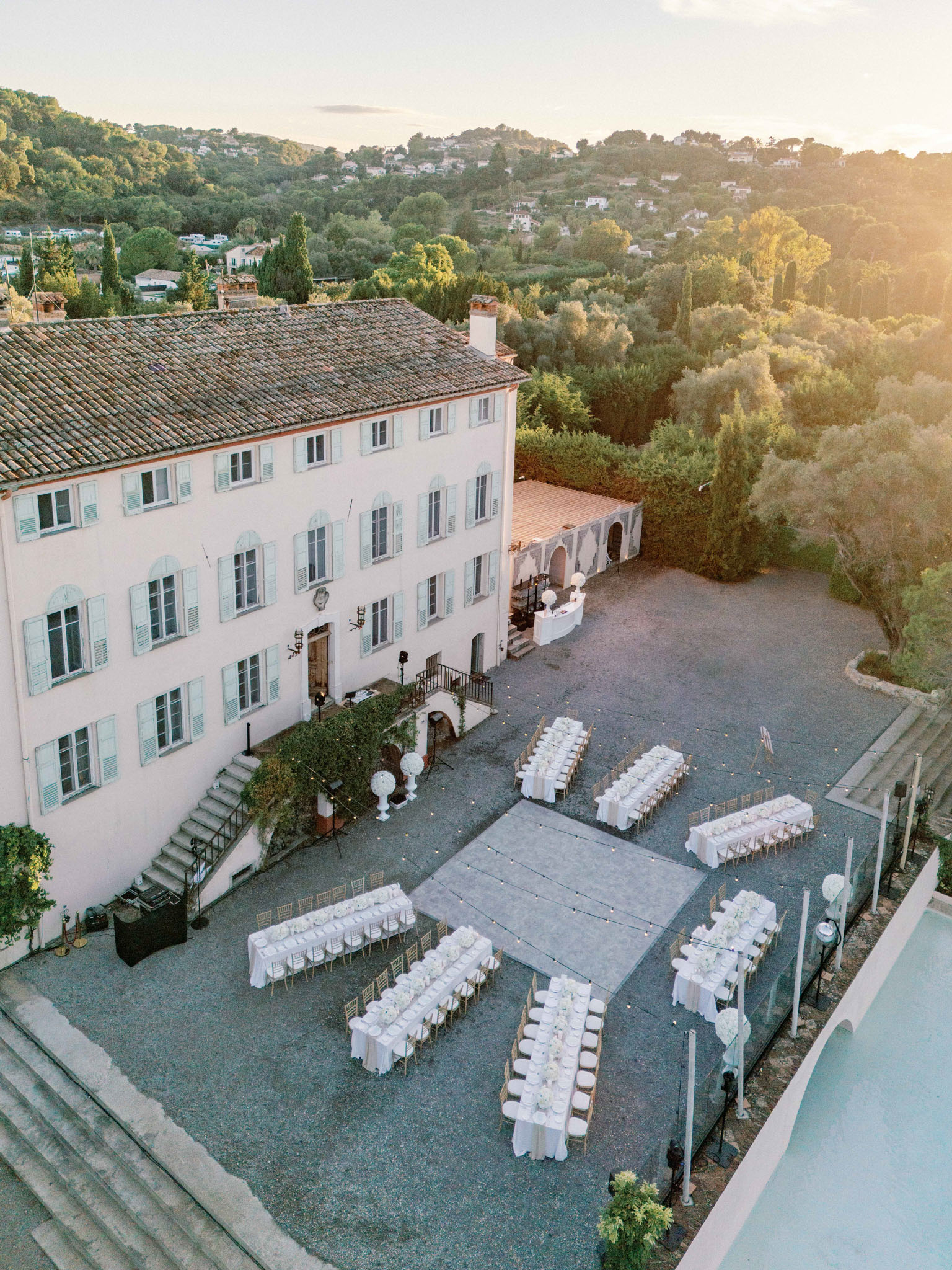 Aerial view of outdoor wedding reception with long white tables and gold chairs in Provencal bastide courtyard