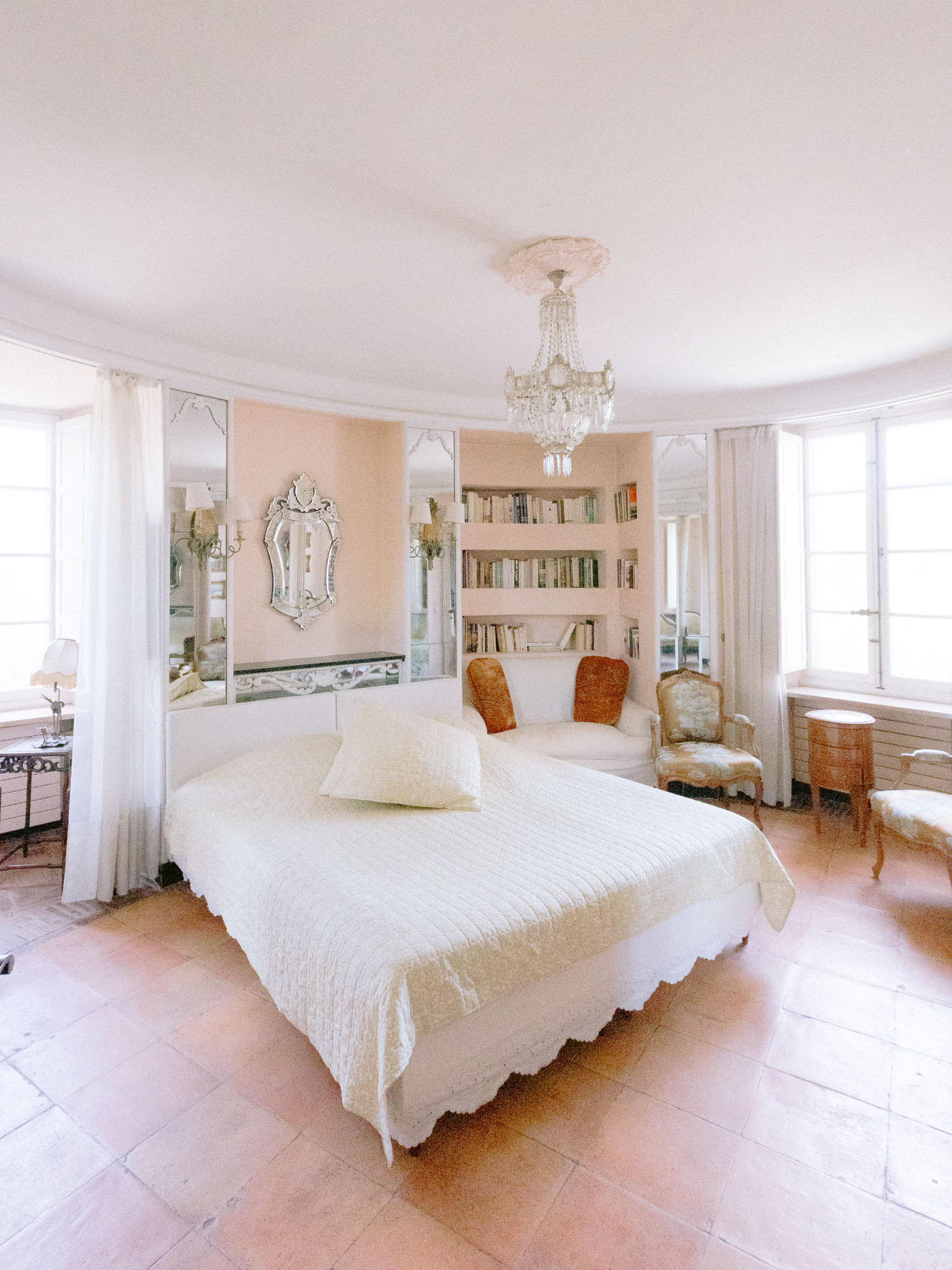 Chateau bridal suite with blush pink walls, crystal chandelier, quilted ivory bed, and curved bookcase wall