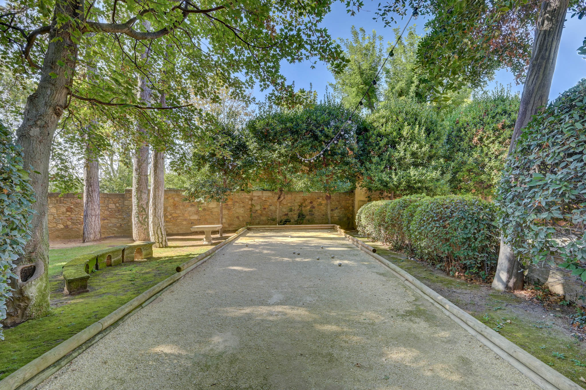 Petanque court with metal boules bordered by hedges and stone walls with string lights at French wedding venue