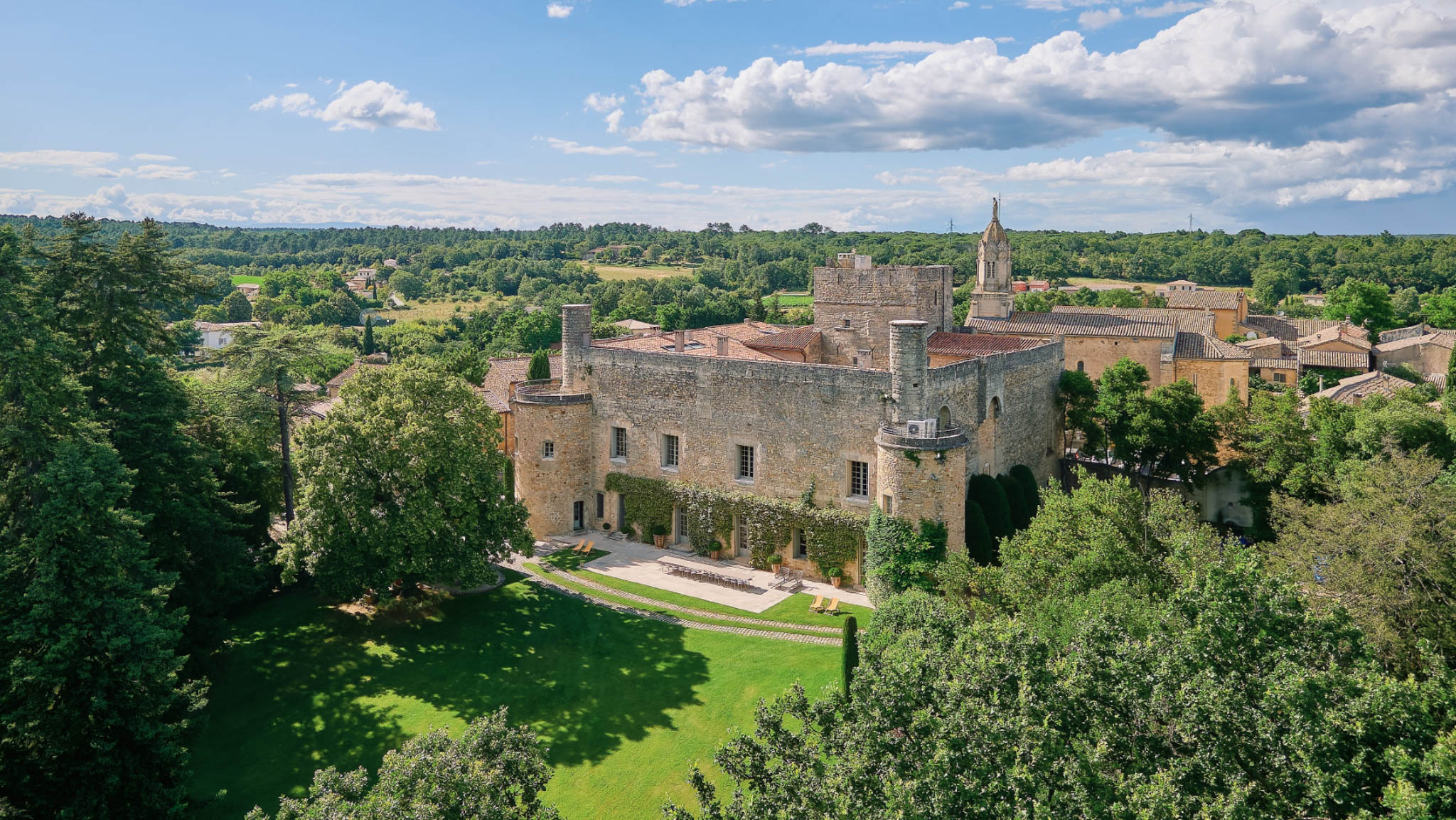 Aerial view of a medieval stone chateau with corner towers and terracotta roofs in a Provencal village