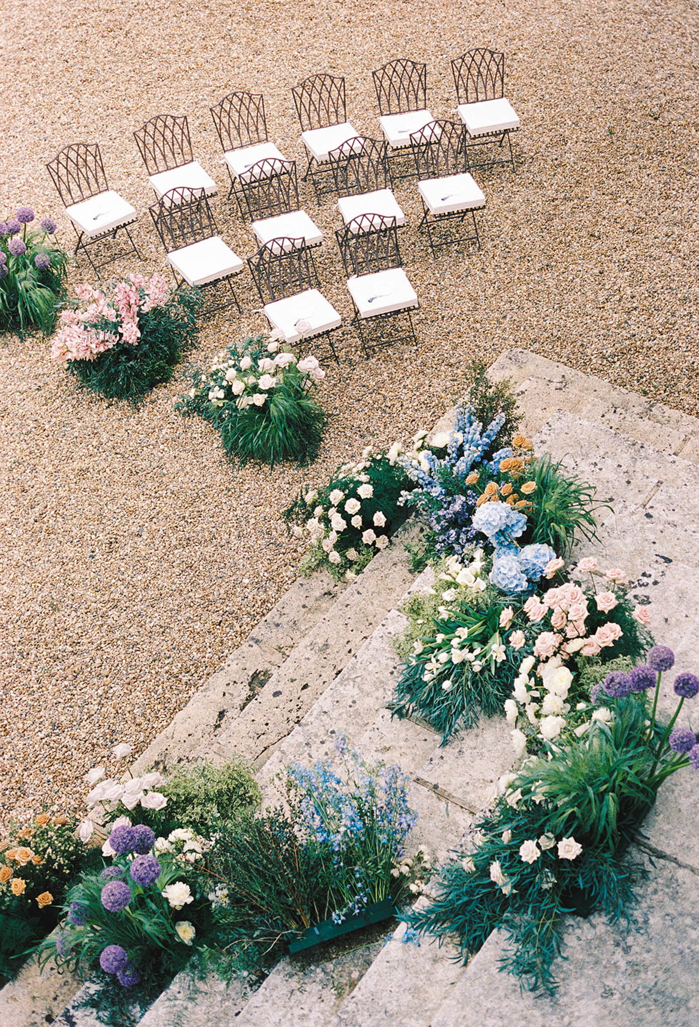 Aerial view of wedding ceremony setup with black chairs and colorful floral arrangements on gravel surface