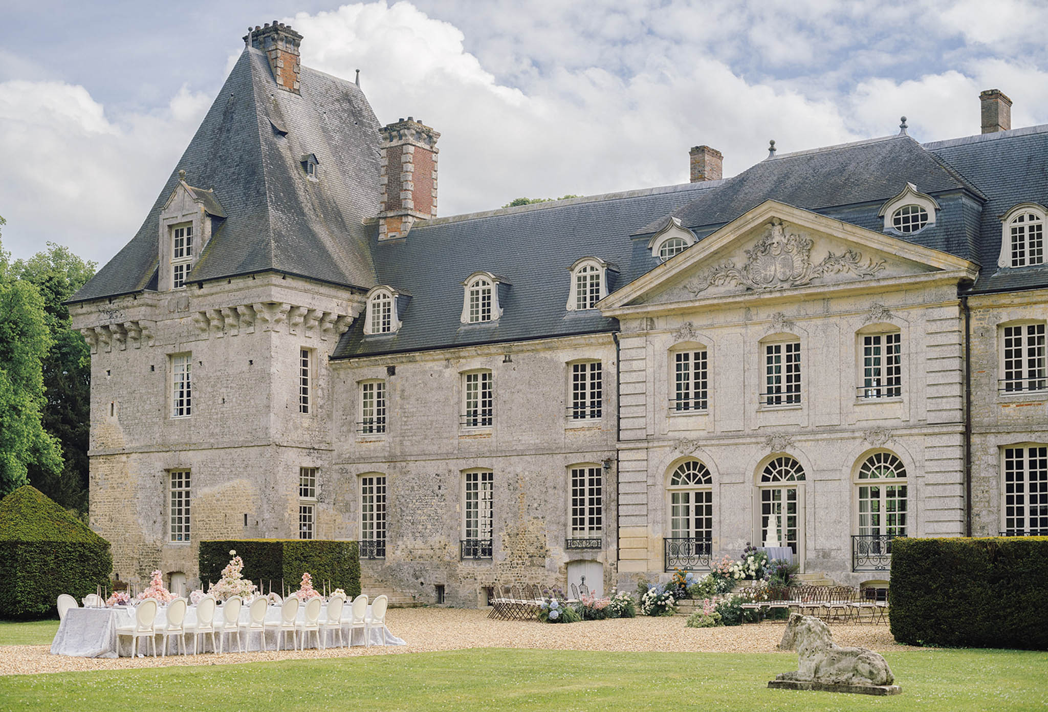 Reception setup on château grounds with white tables and chairs on manicured lawn