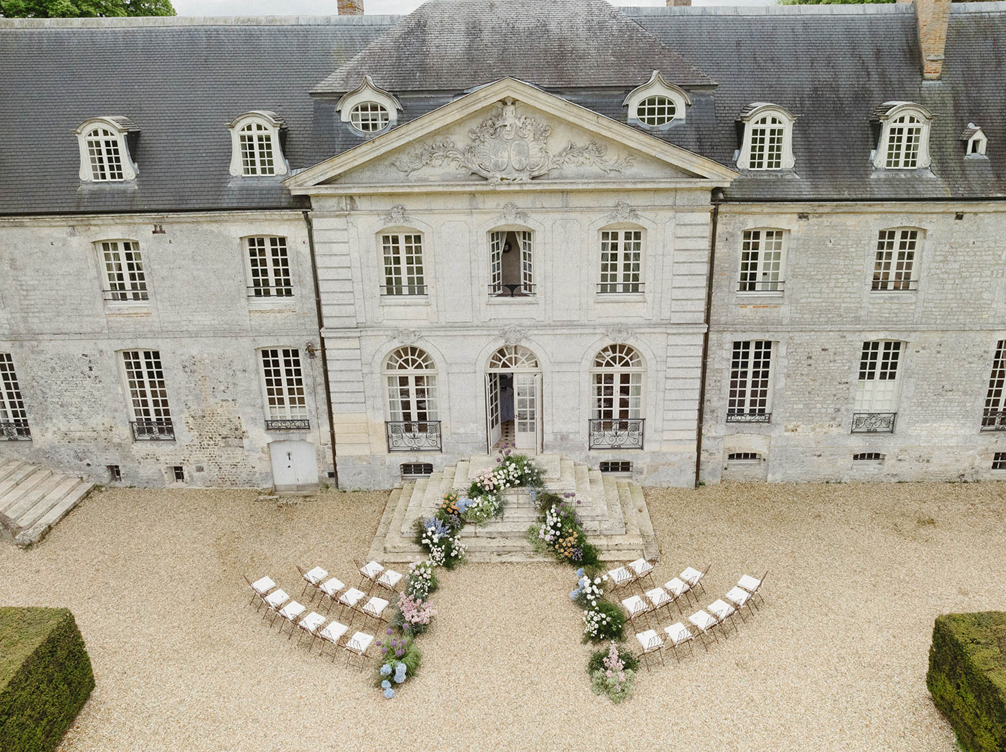 Aerial view of wedding ceremony setup in château courtyard with white chairs and floral arrangements