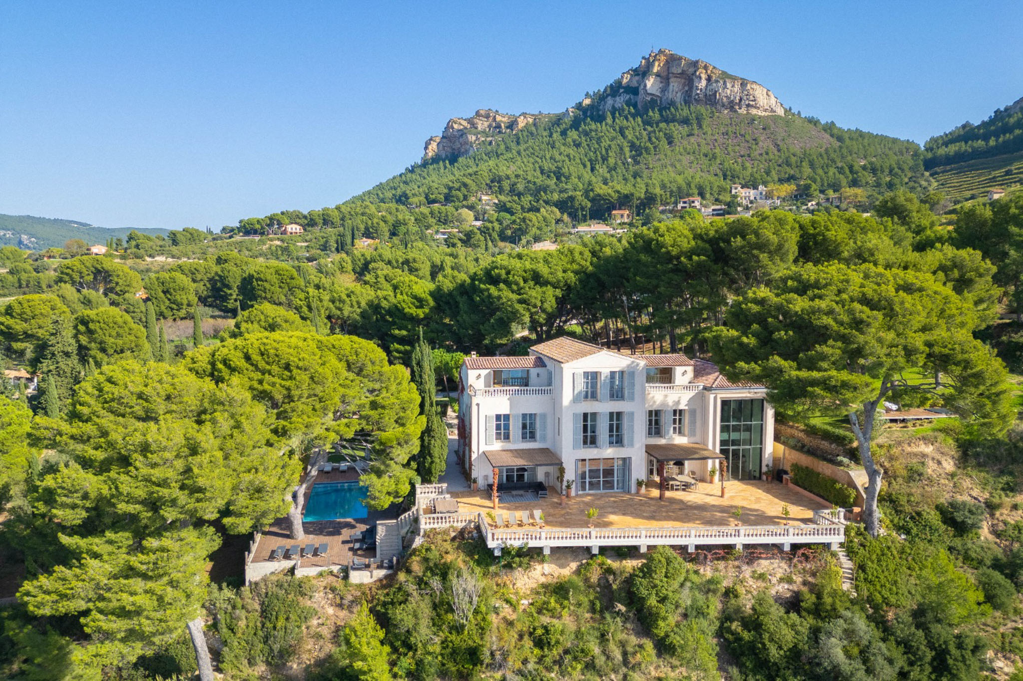 Aerial view of white Provencal villa with terracotta roof, swimming pool, and stone terrace on a wooded hillside