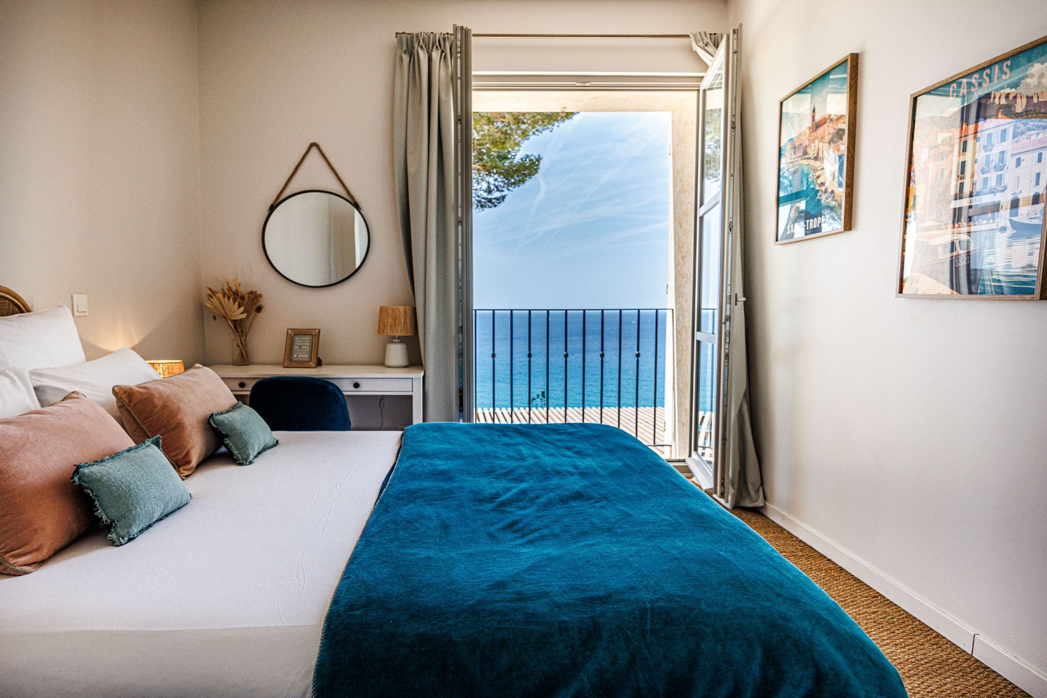 Coastal venue bedroom with white linens, teal throw, dried pampas grass, and French doors opening to sea view balcony