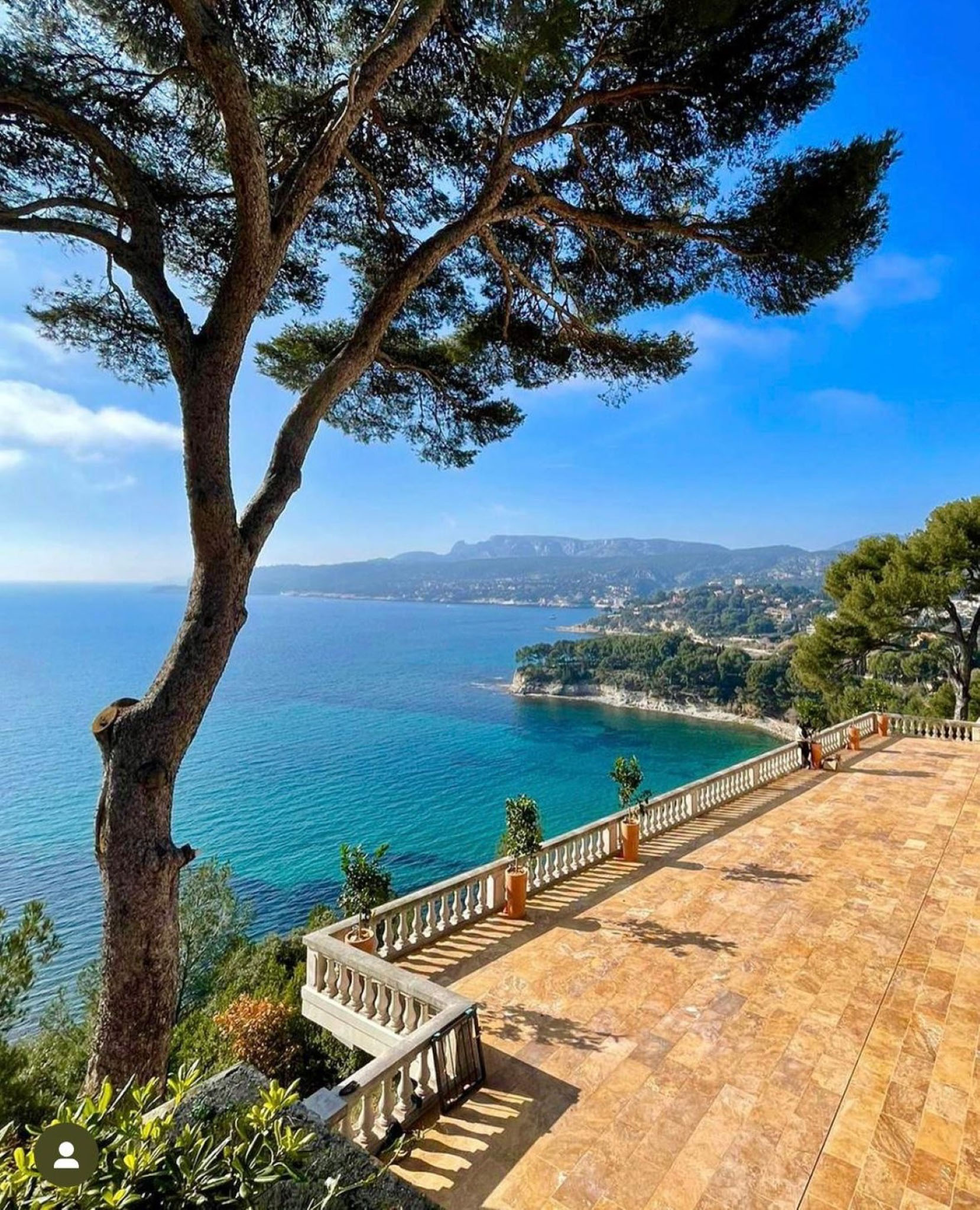 Stone terrace with white balustrade and terracotta pots overlooking turquoise coastal bay on the French Riviera