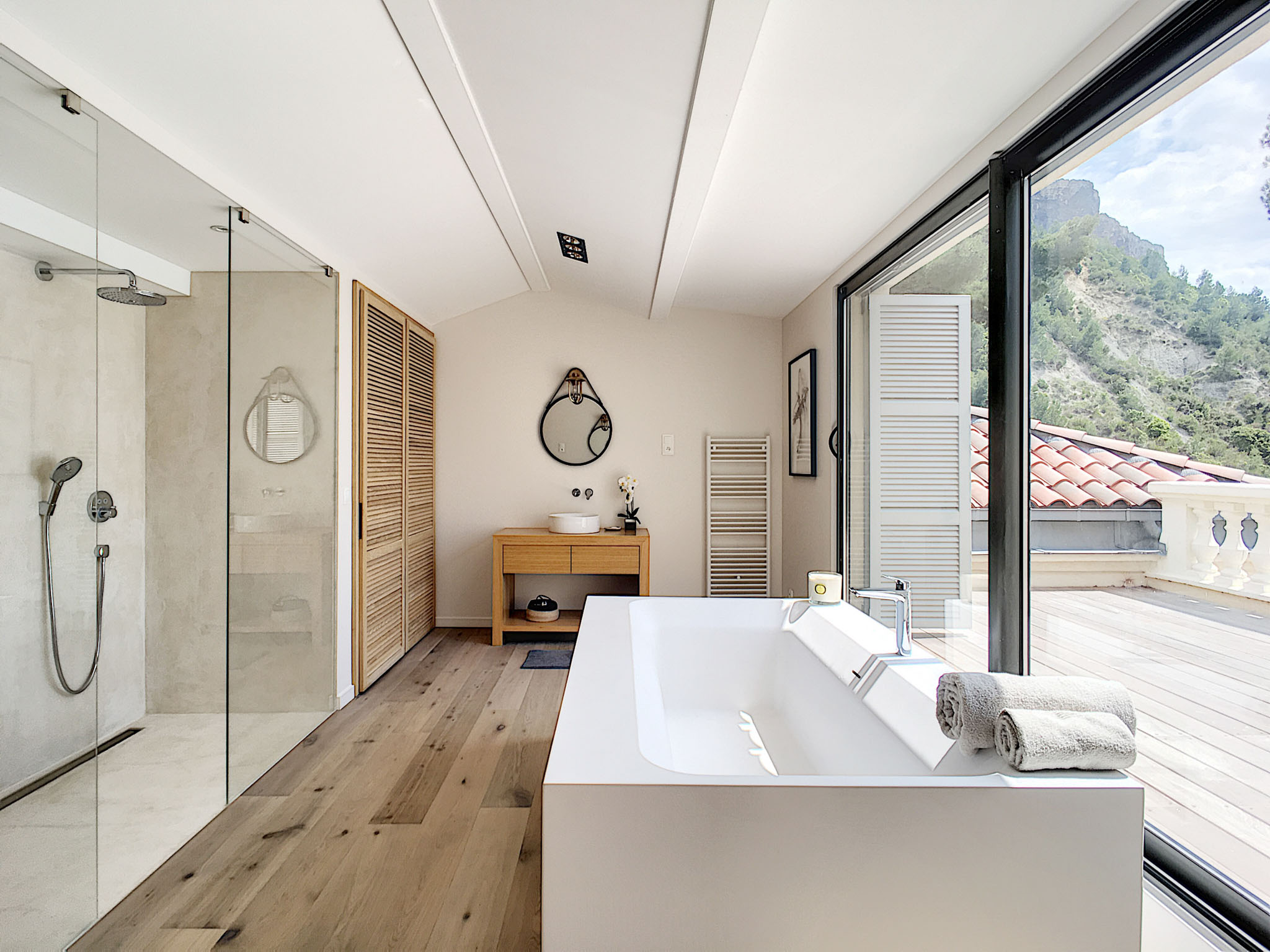 Modern venue bathroom with freestanding bathtub, walk-in shower, oak vanity, and glass door opening to terrace