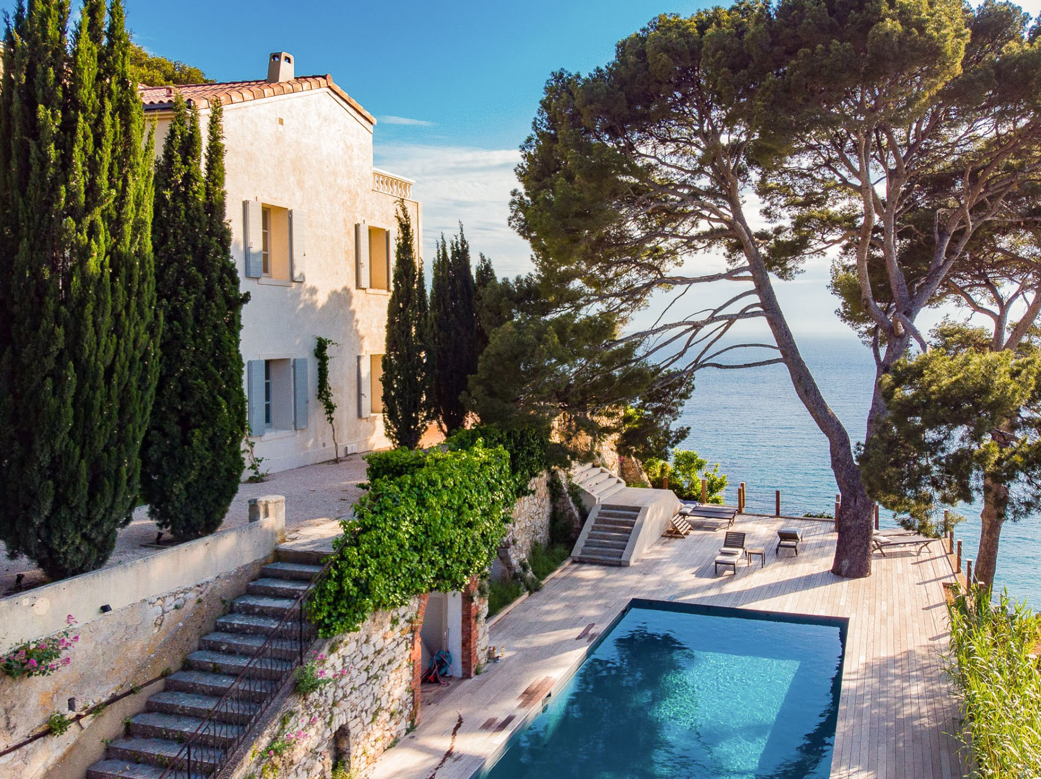 White Provencal villa with terracotta roof, swimming pool on timber deck, and terraced gardens overlooking the sea