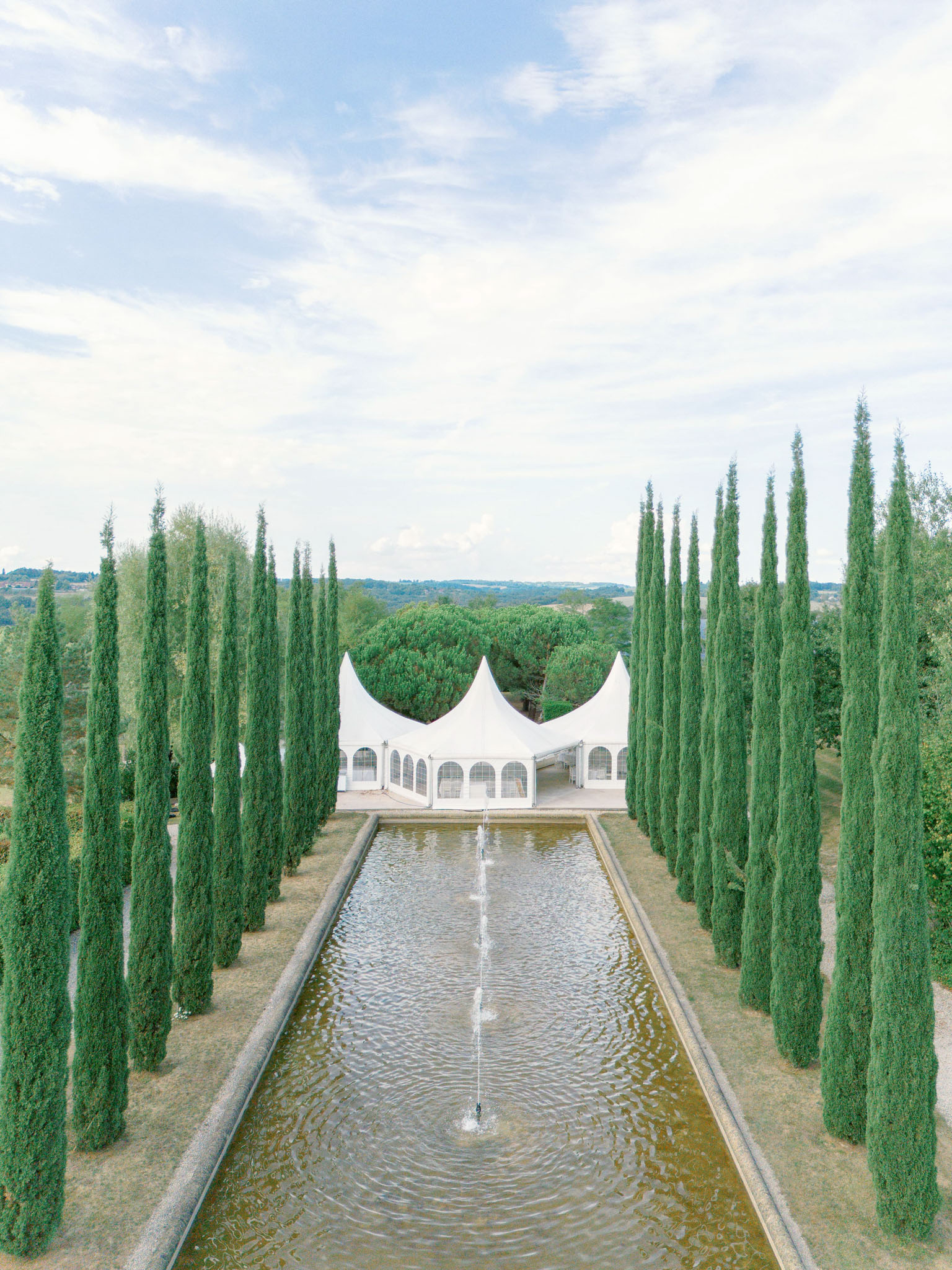 Aerial view of cypress allee with reflecting pool and white pagoda marquee on countryside terrace