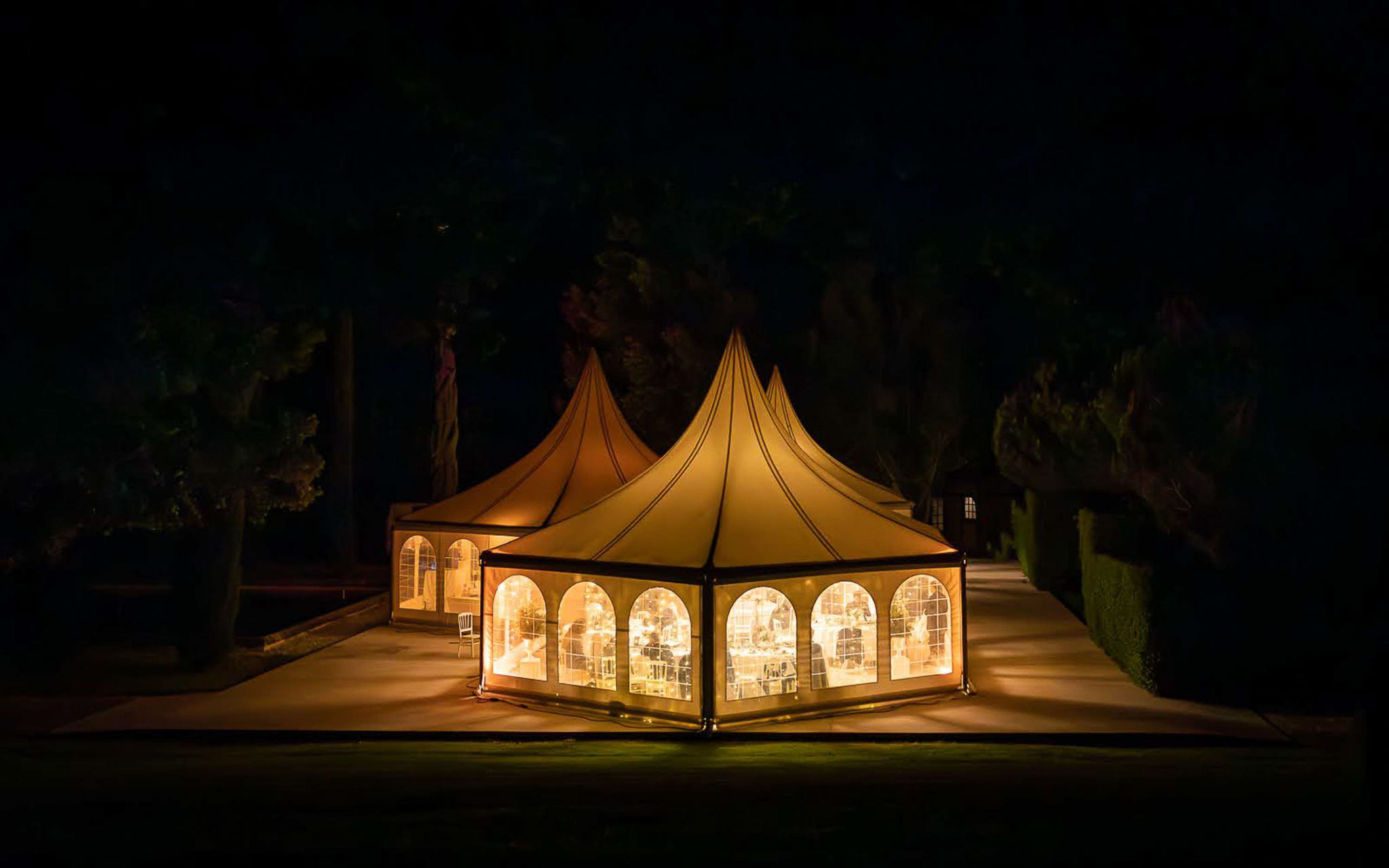 Night view of glowing pagoda marquee tent with guests visible through clear panels at chateau grounds