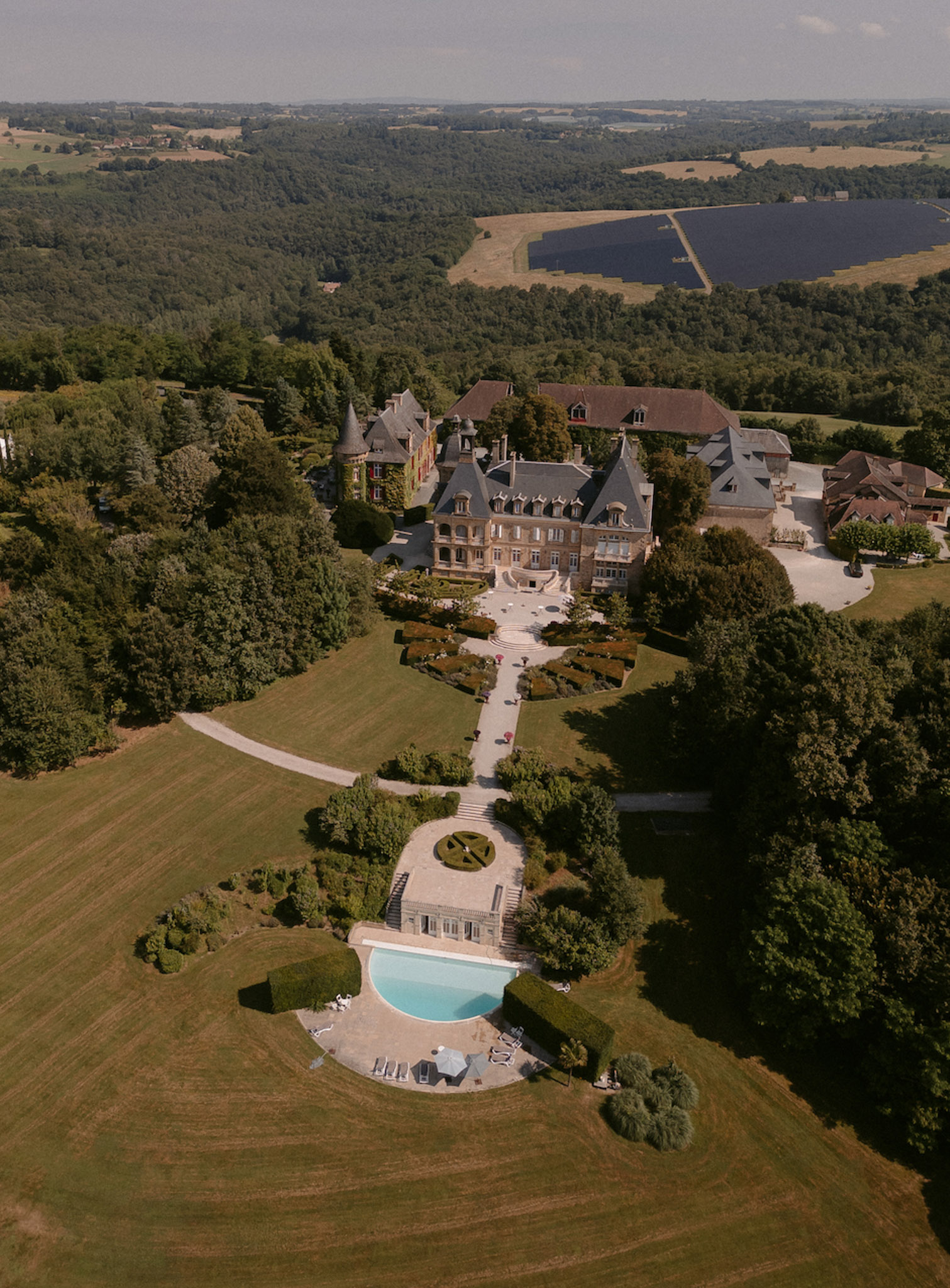 Aerial view of turreted chateau with parterre garden, turquoise pool, and woodland estate grounds
