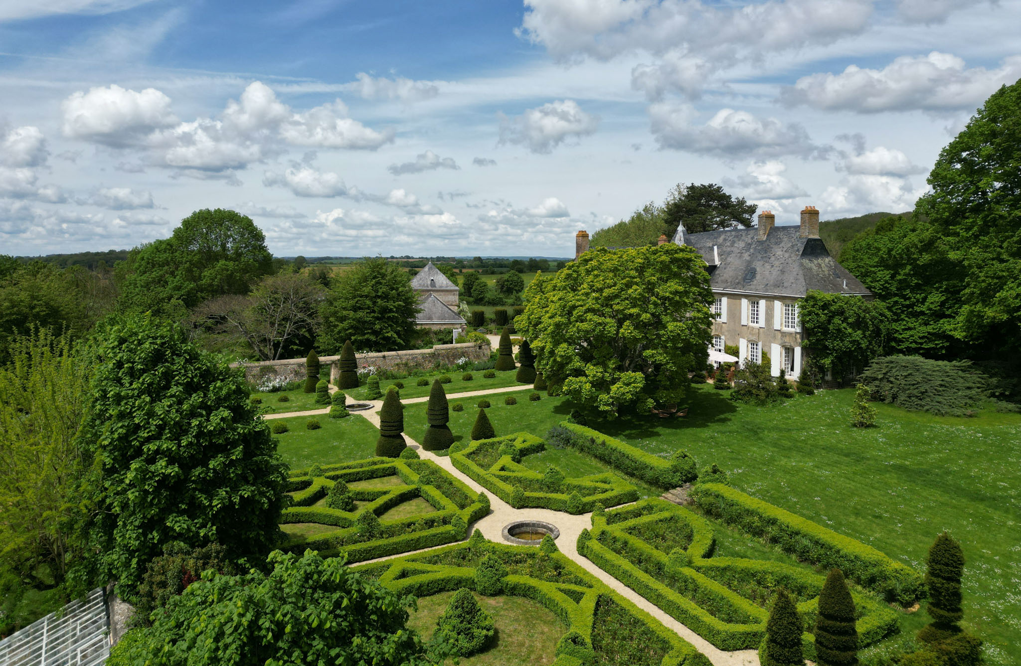 Aerial view of Norman stone manor with formal French parterre garden, clipped box hedges, and open countryside