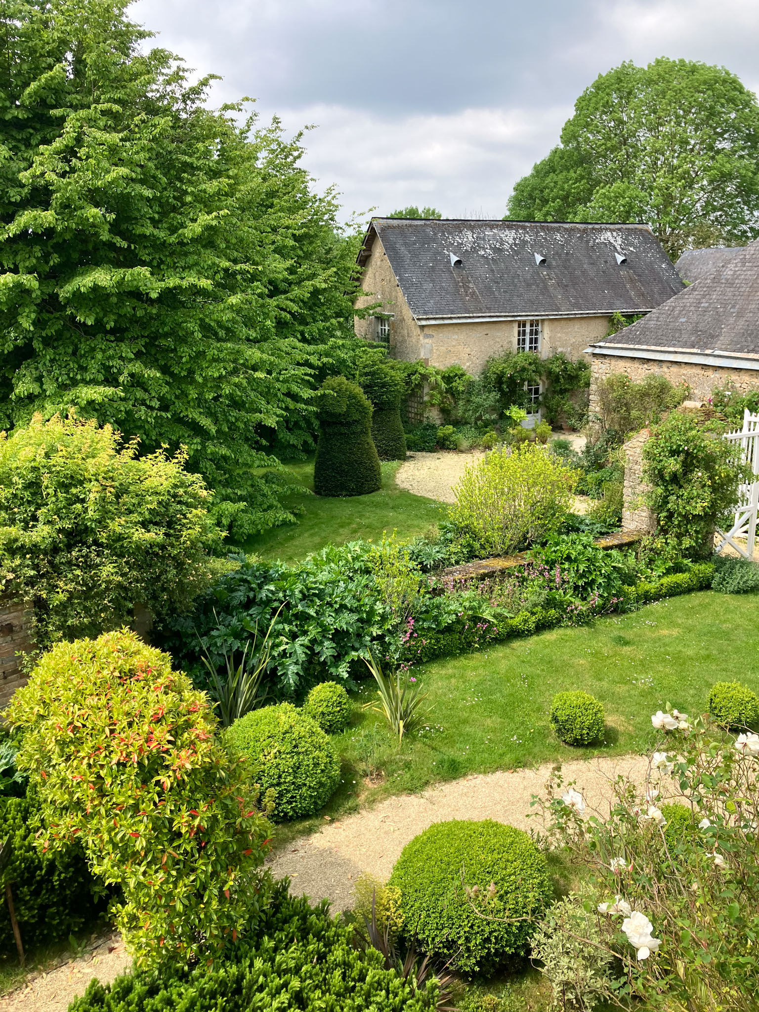 French stone manor house garden with clipped topiaries, gravel paths, white roses, and wooden bench