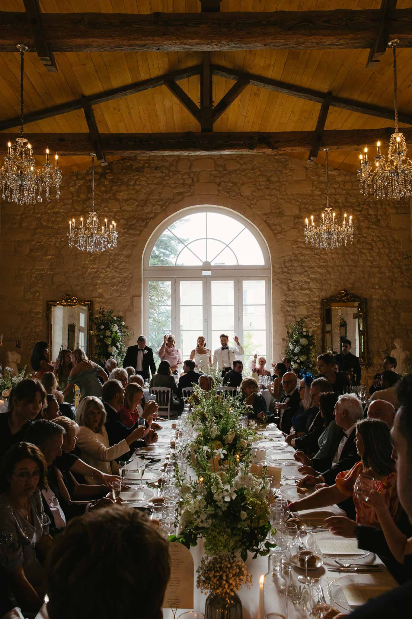 Wedding reception dinner service with guests at long banquet table in rustic stone barn venue