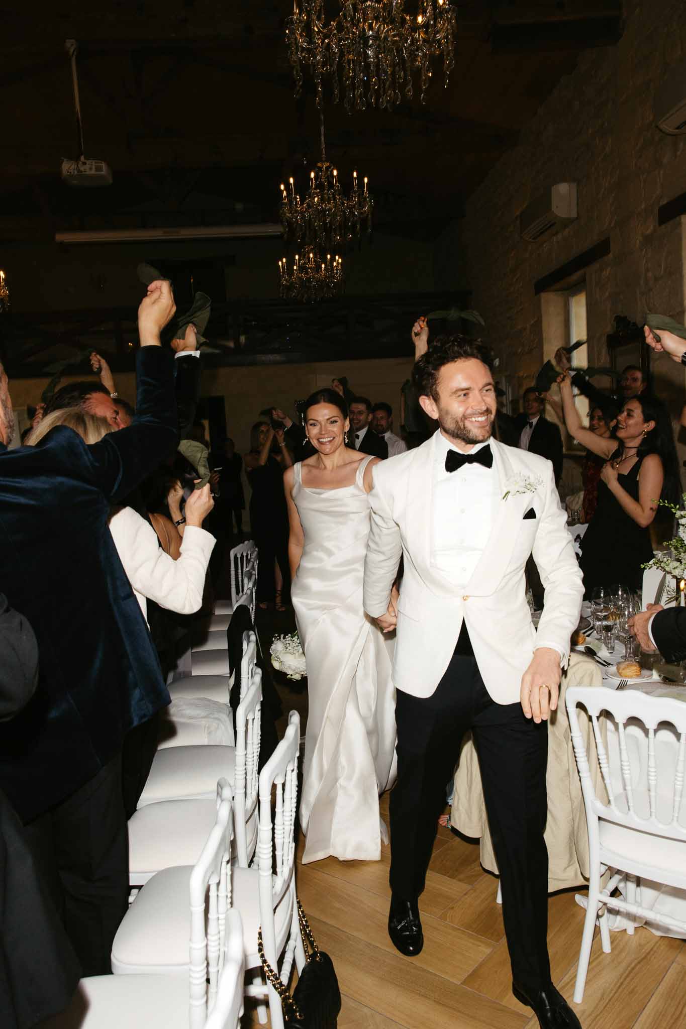 Bride and groom walking down aisle during first dance in elegant ballroom with crystal chandeliers