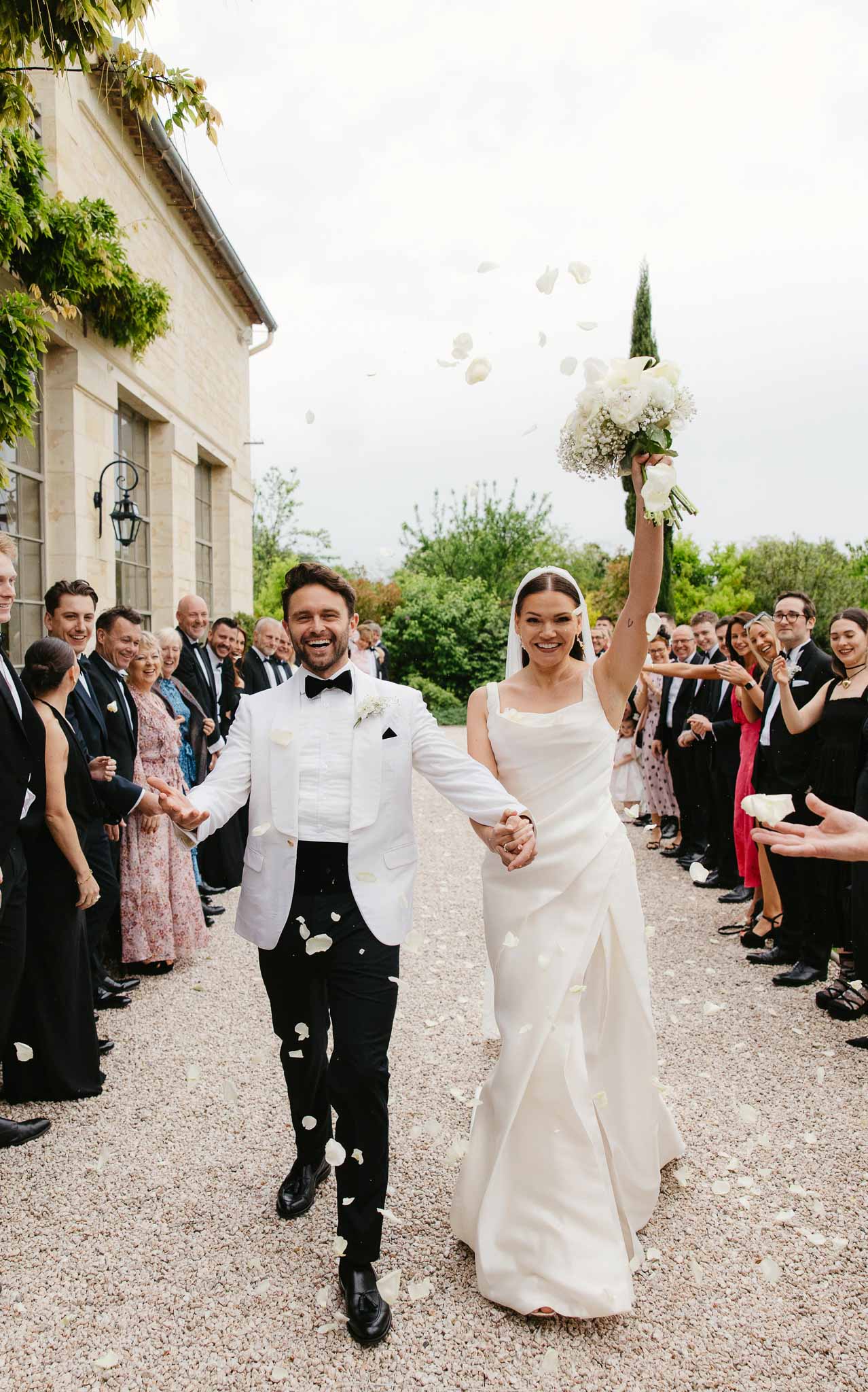 Bride and groom walking down courtyard path during wedding recessional with guests tossing petals