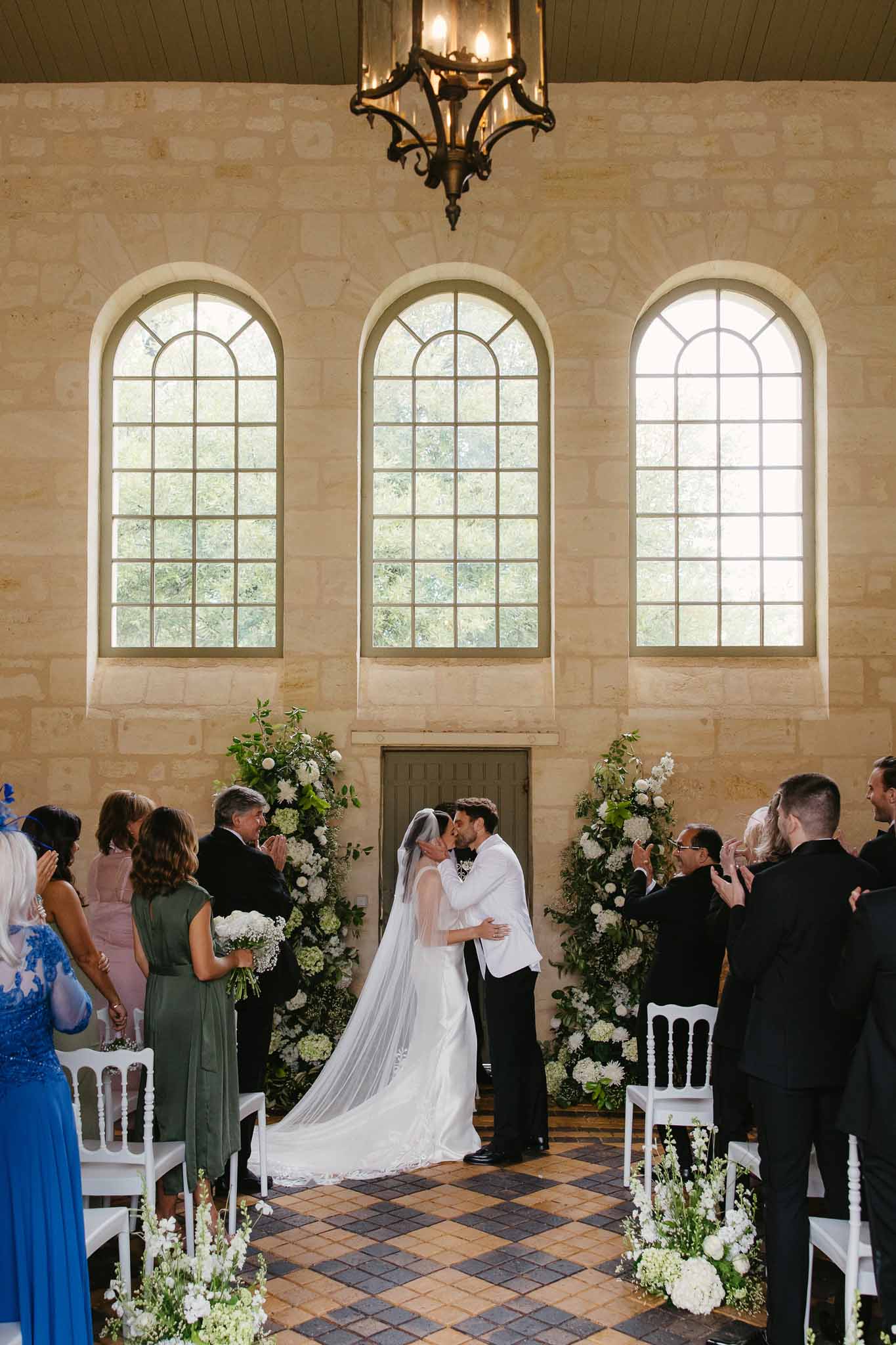 Couple's first kiss during wedding ceremony in stone chapel with arched windows