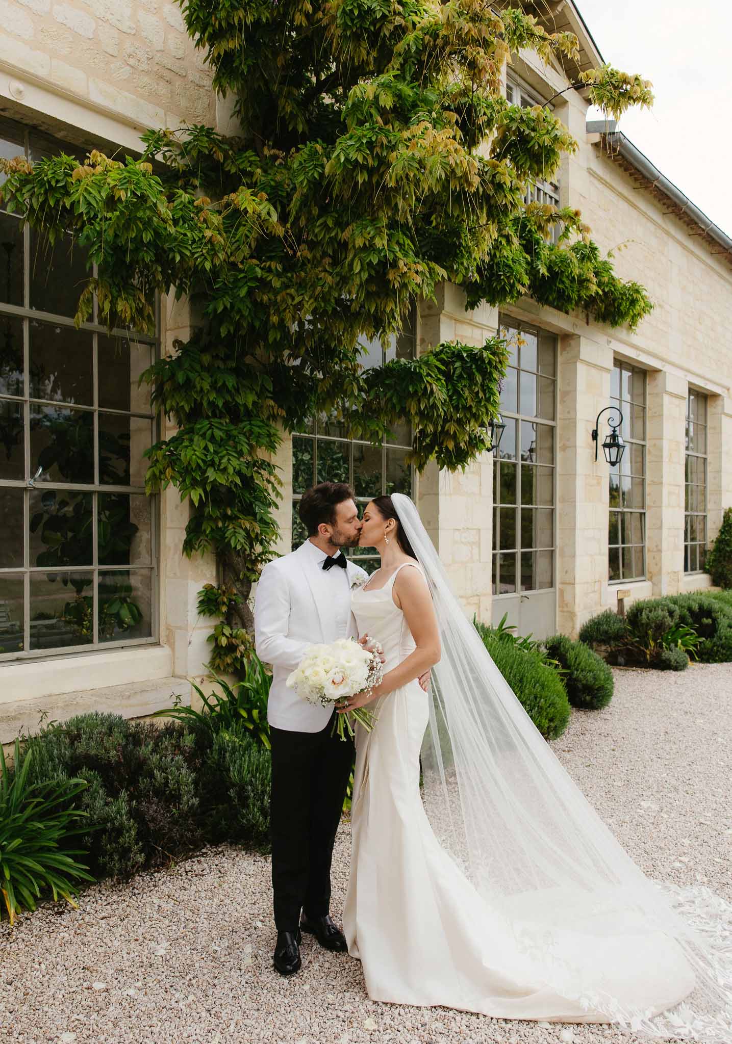 Bride and groom kissing in romantic portrait at ivy-covered stone courtyard