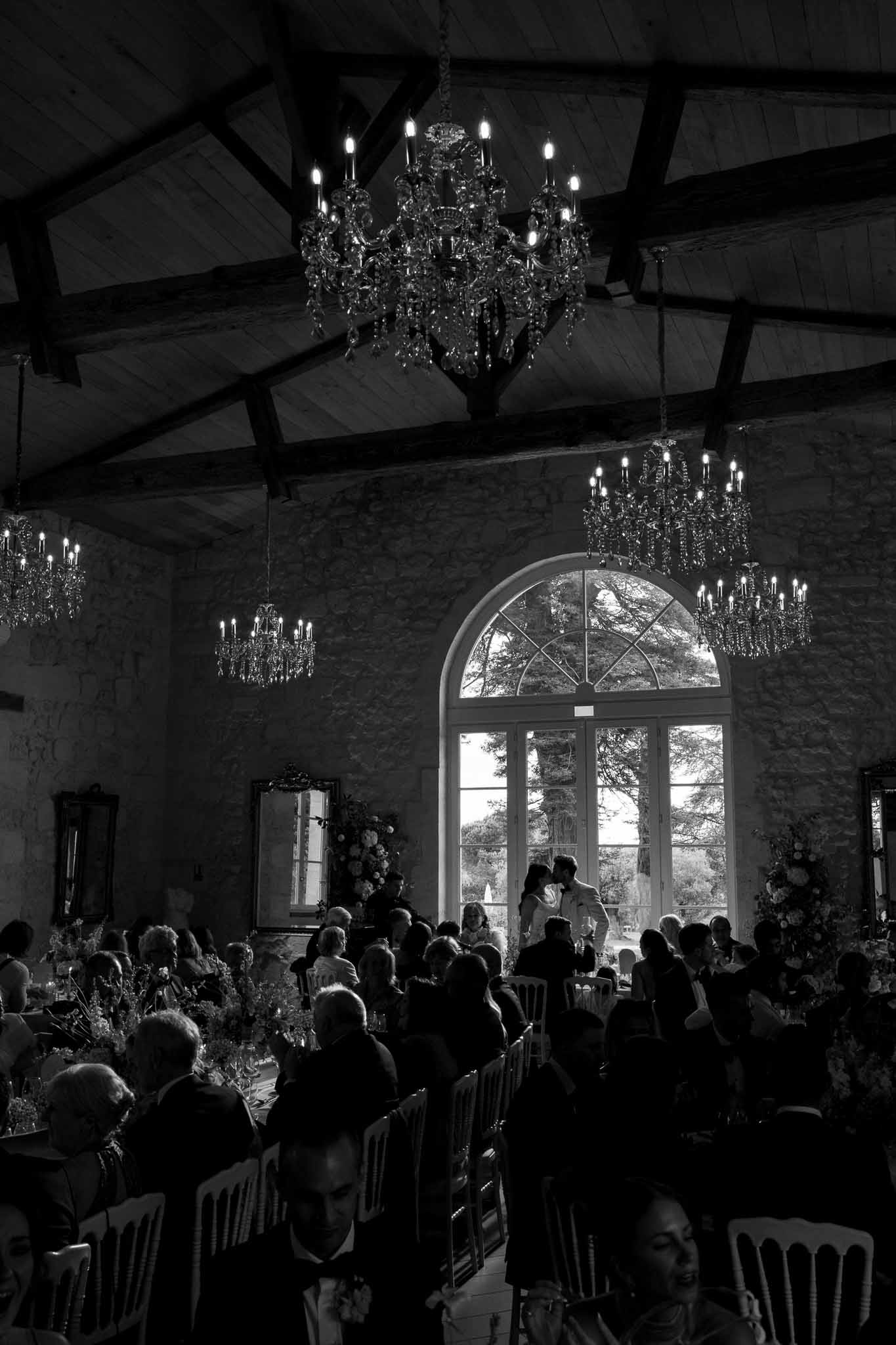 Wedding ceremony in stone barn venue with exposed beams and crystal chandeliers