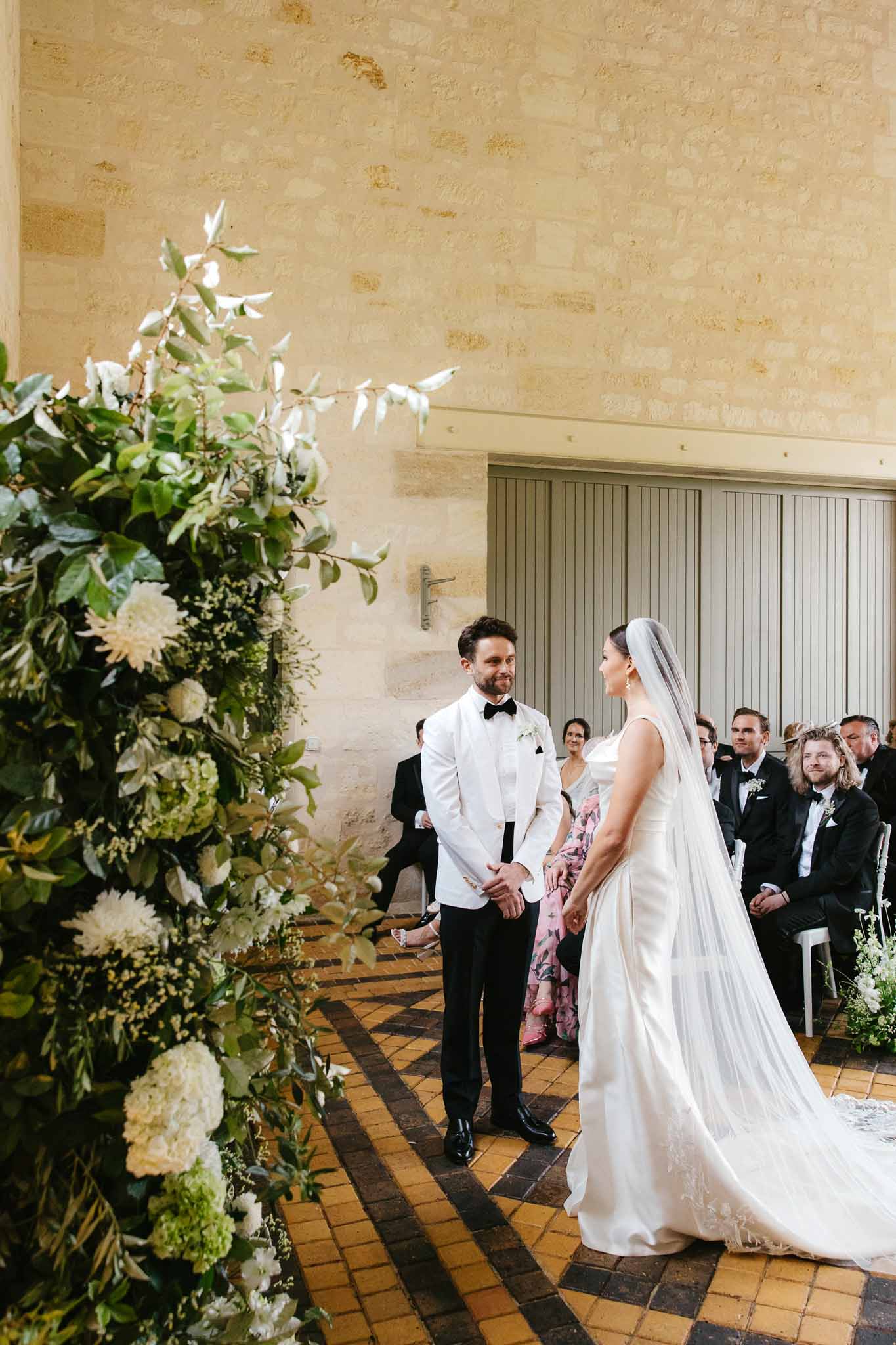 Indoor wedding ceremony with bride and groom exchanging vows in stone-walled room with guests