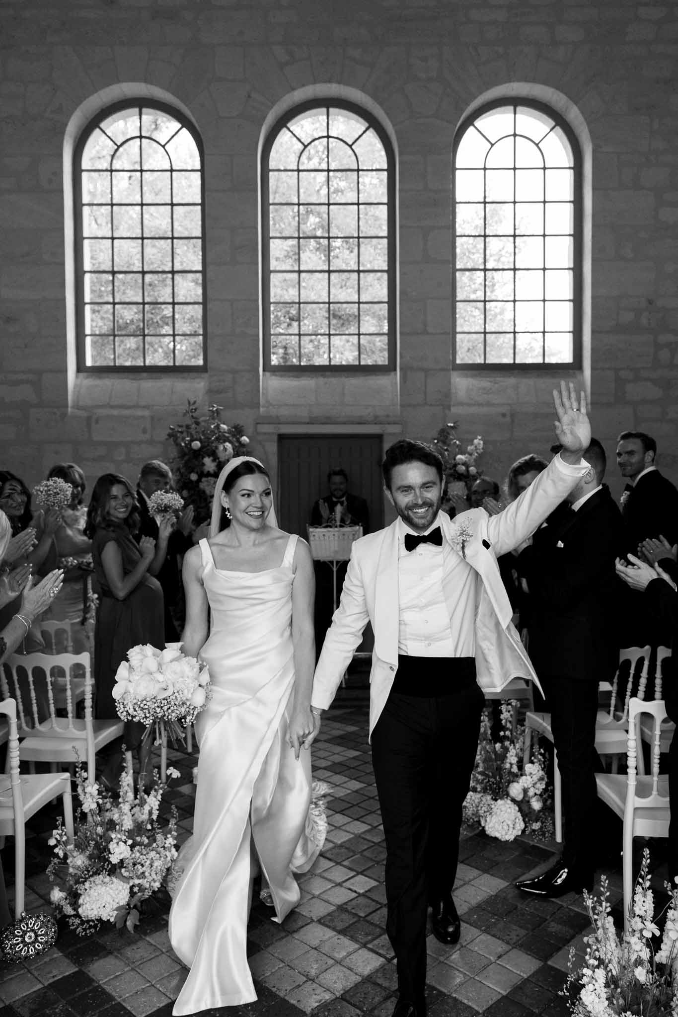 Newlyweds walking down aisle after ceremony in classical chapel with arched windows