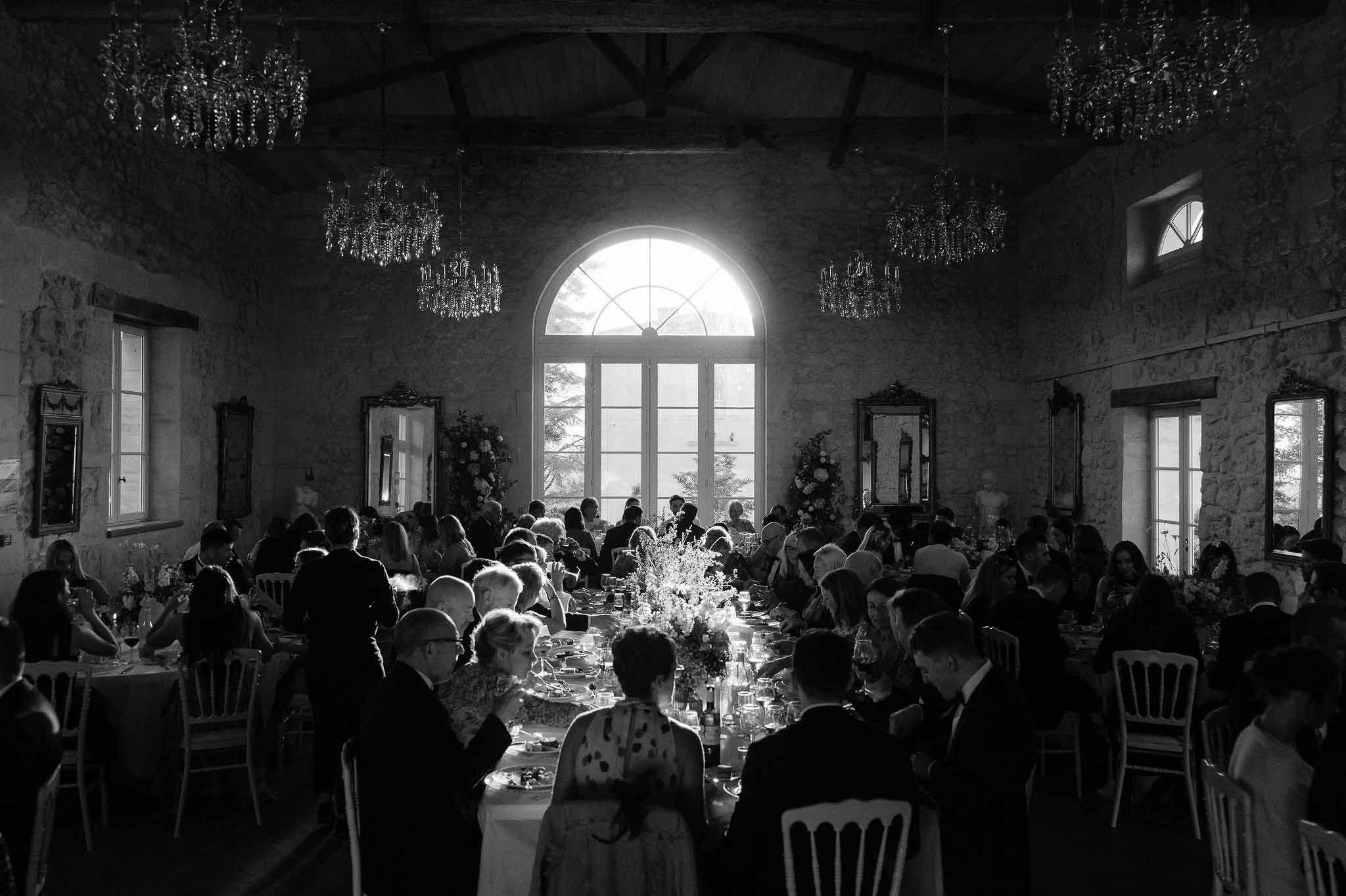 Wedding reception dinner in industrial warehouse venue with crystal chandeliers and long banquet table
