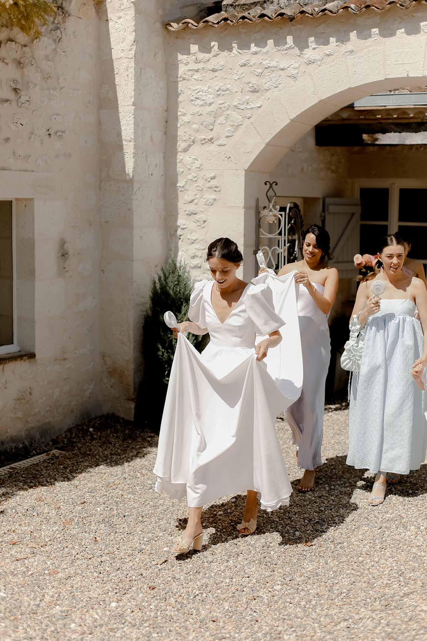 Bride and bridesmaids walking through Mediterranean courtyard with stone archways and terracotta tiles