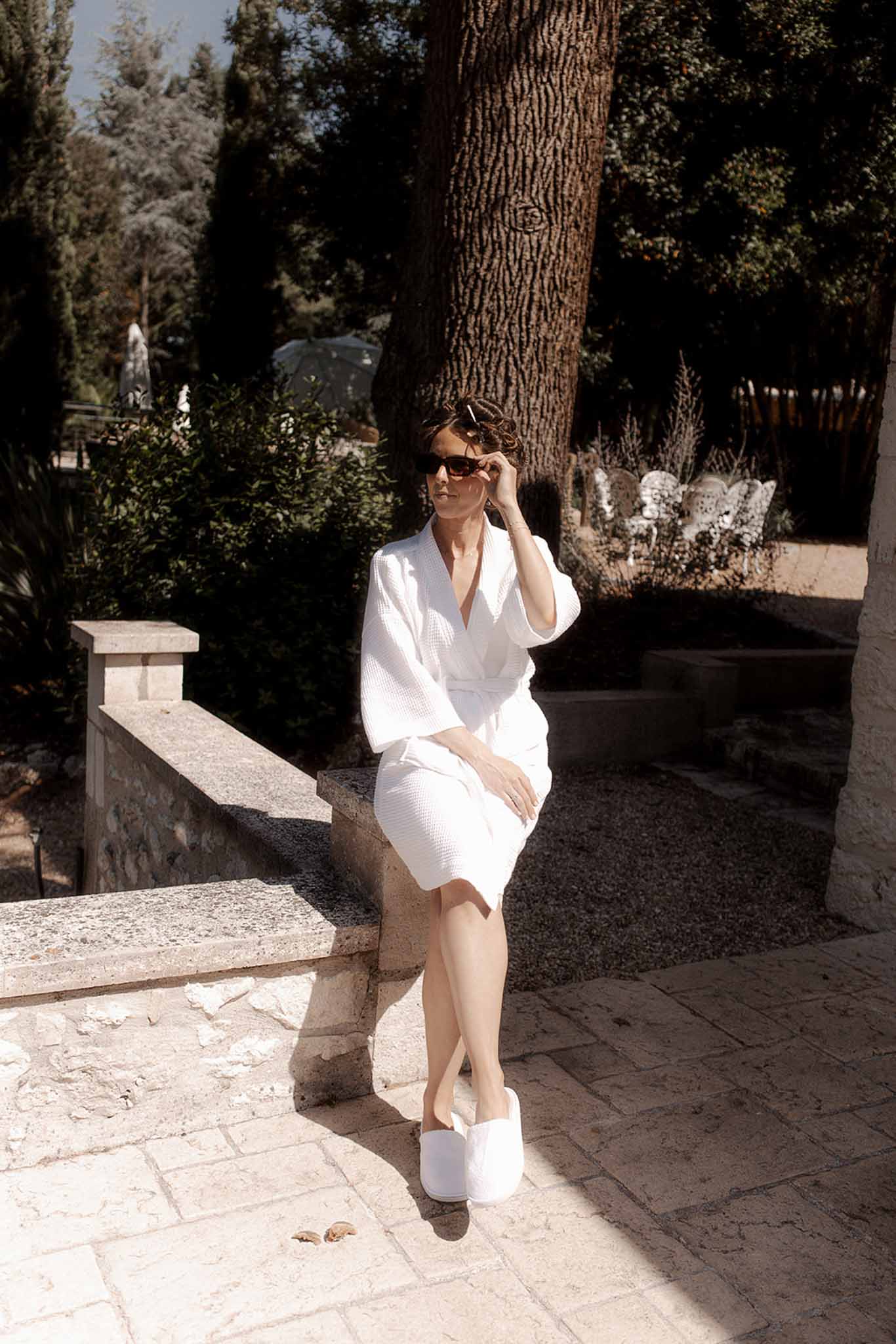 Woman in white dress seated on stone bench in Mediterranean garden setting