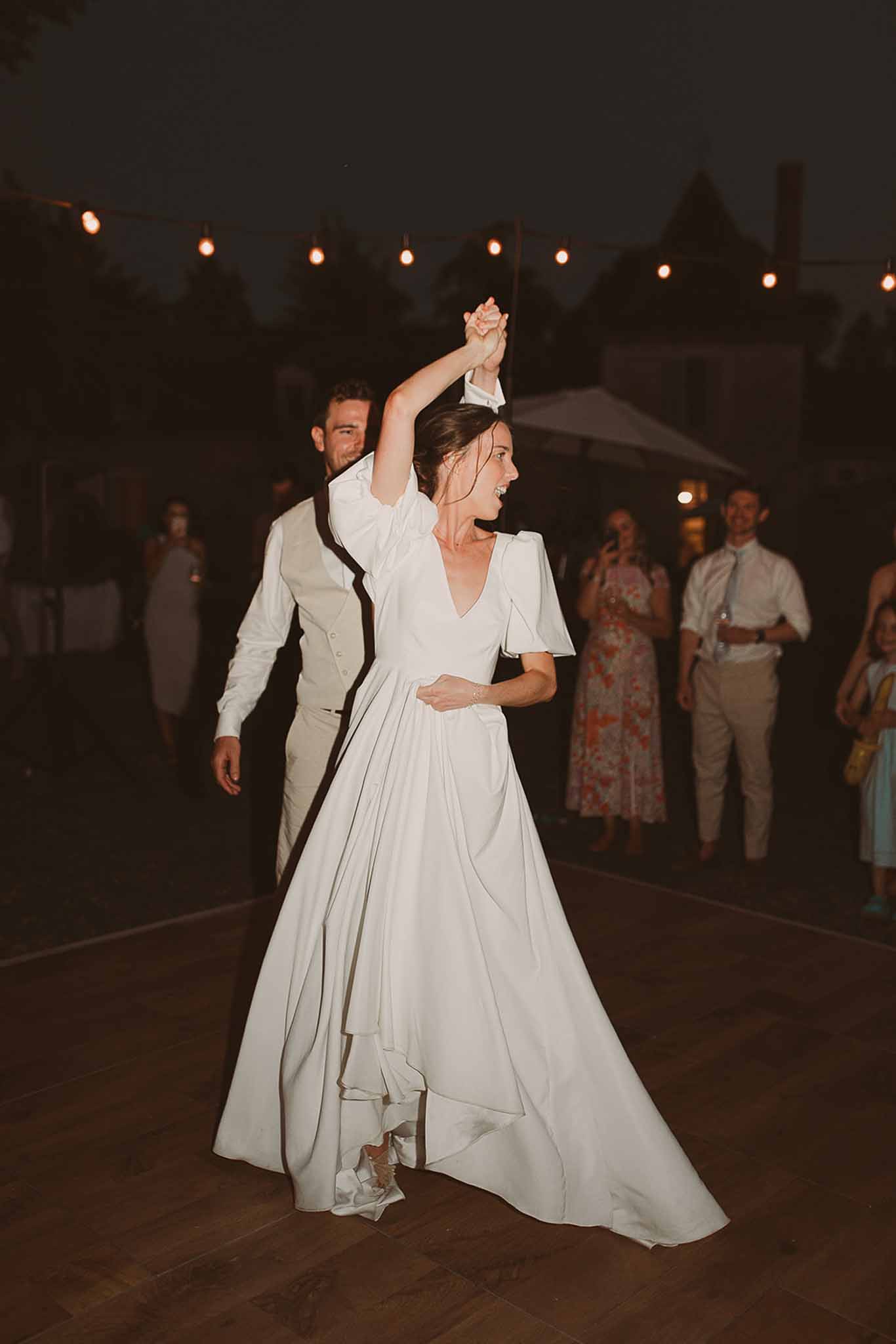 Couple's first dance at outdoor evening wedding reception with string lights and guests